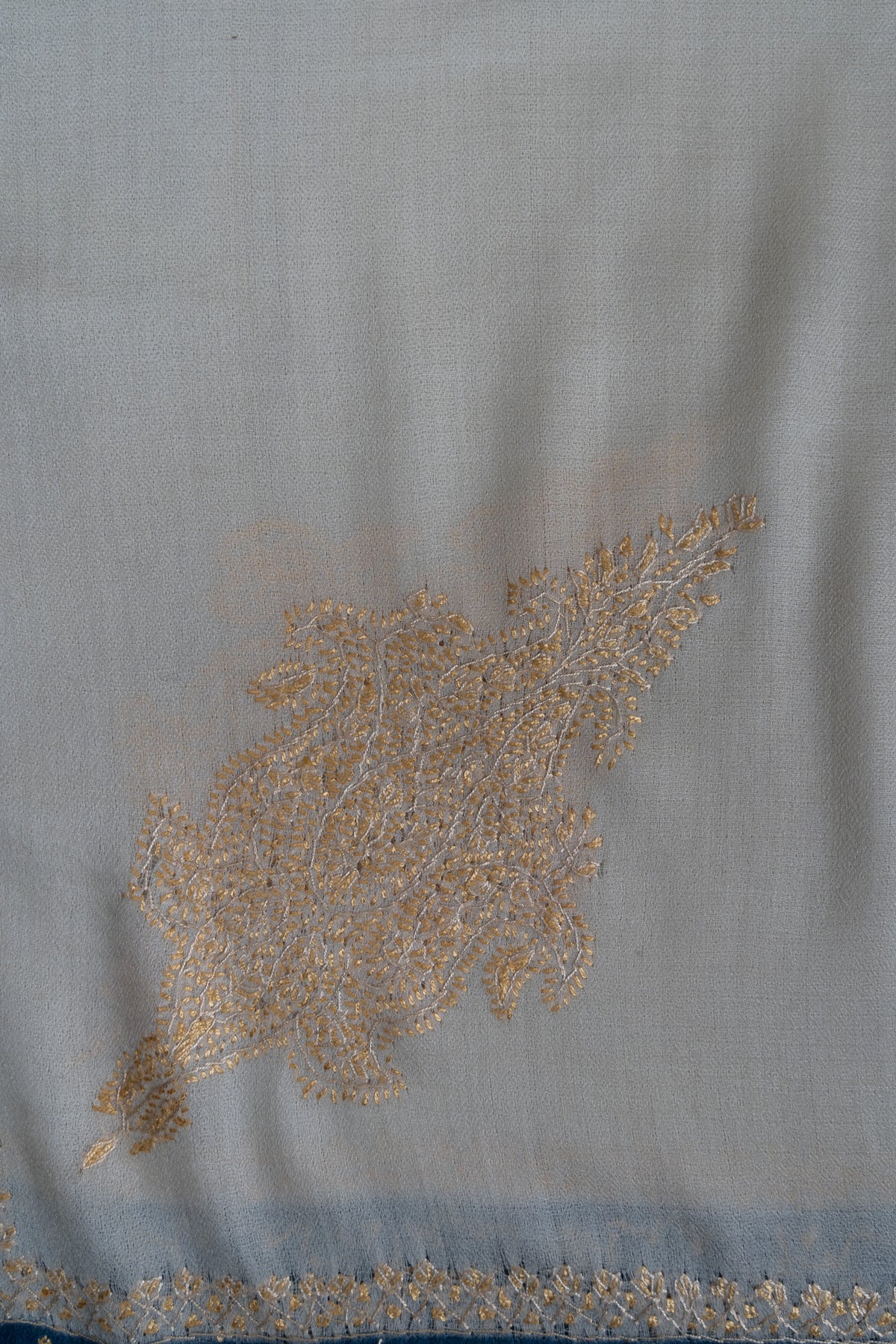 Close-up of a pale golden Sozni corner motif filled with fine floral stitching on ivory shawl fabric
