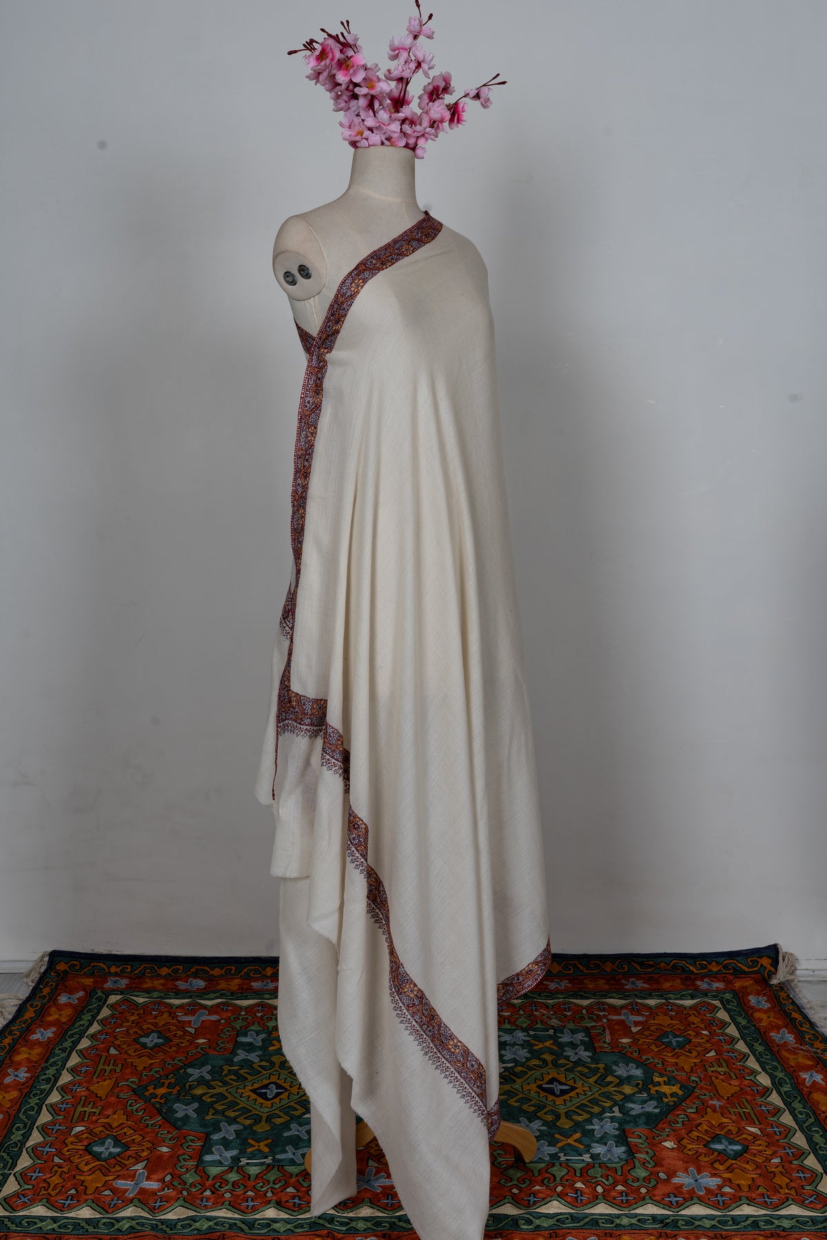 Full view of the ivory Merino wool shawl draped on a mannequin with narrow burgundy and orange borders