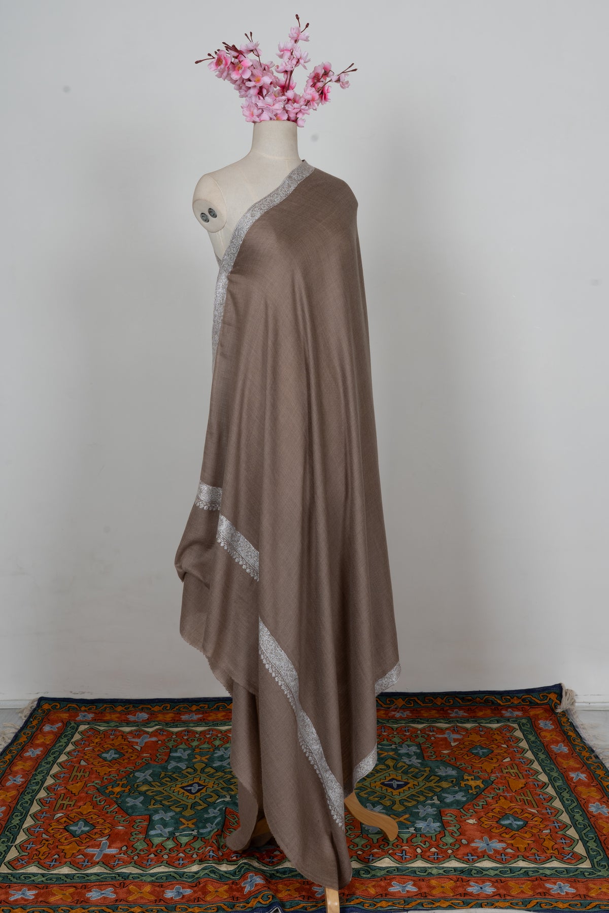 Full view of a walnut-brown Merino wool shawl on a mannequin, showing a plain centre and silver embroidered borders