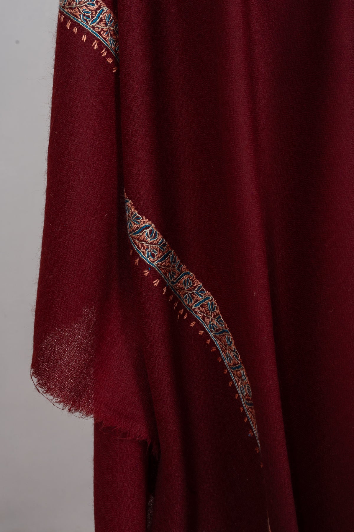 Draped detail of the maroon shawl showing a teal and beige border across soft folds
