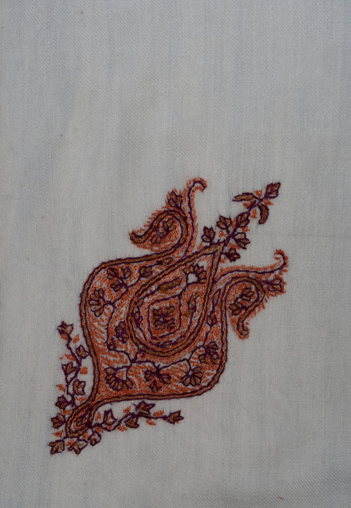 Close-up of a cinnamon and copper Sozni corner motif with dark outlines and small floral details on ivory fabric
