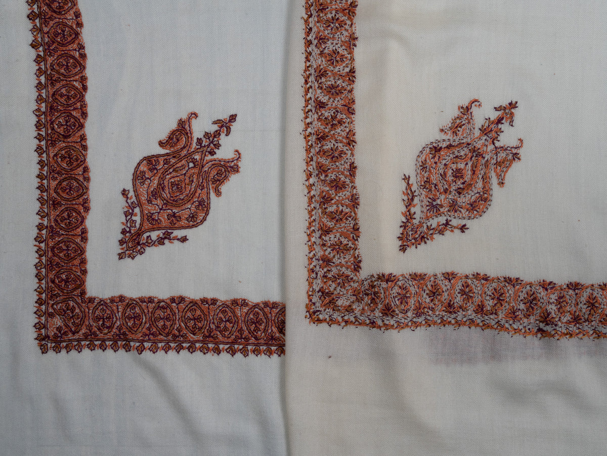 Folded ivory rumal showing both sides of cinnamon-toned Sozni corner motifs and floral borders