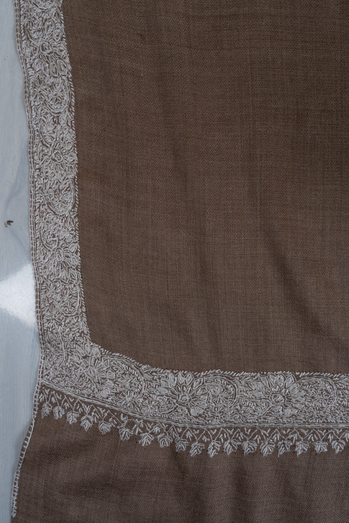 Corner of a walnut-brown Merino wool shawl showing its silver floral border and fine leafy edging