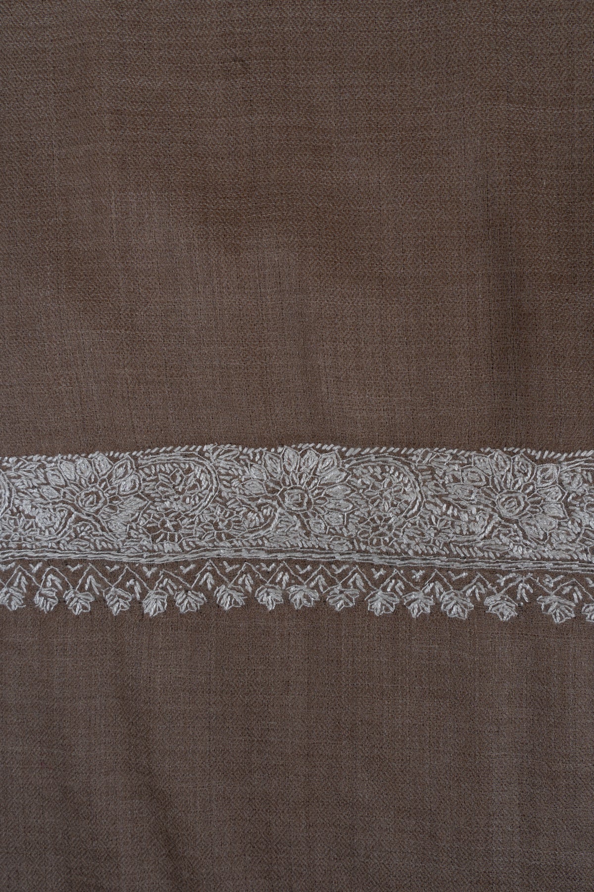 Close-up of silver flowers and scrolling foliage in the end border of a walnut-brown Merino wool shawl