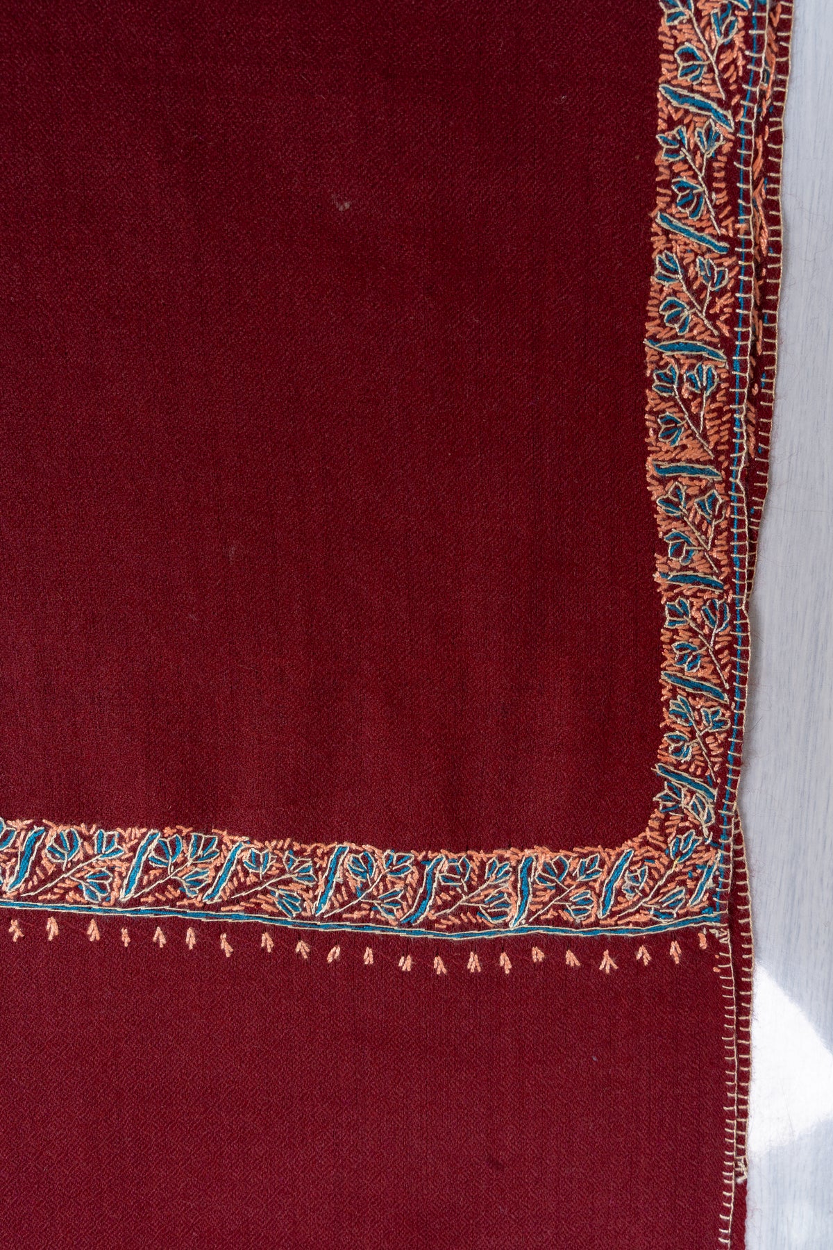 Corner detail of the maroon shawl with teal and beige leafy embroidery and tiny hanging stitches