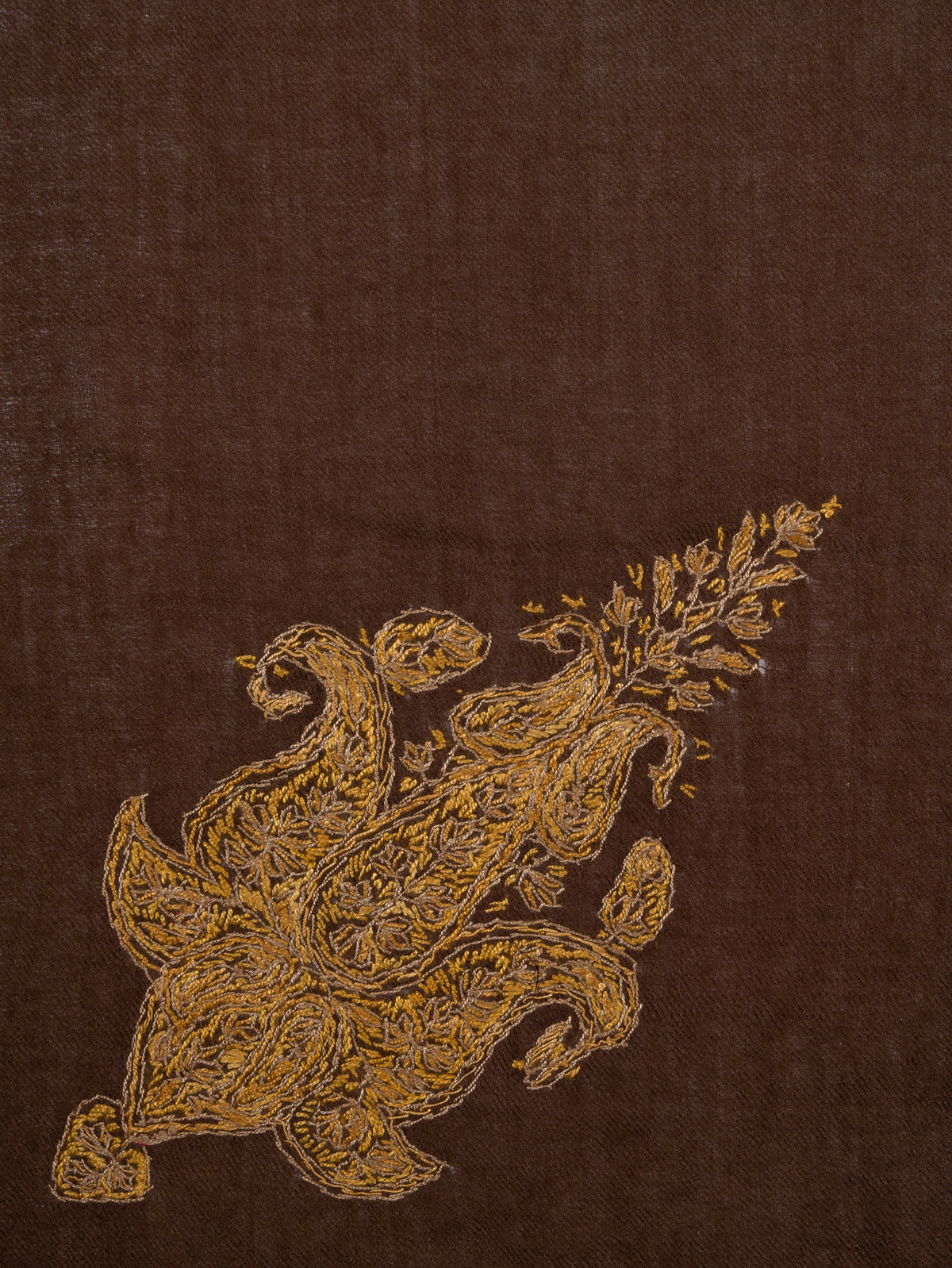 Close-up of a golden paisley motif with curling leaves and fine floral stitches embroidered on umber-brown fabric