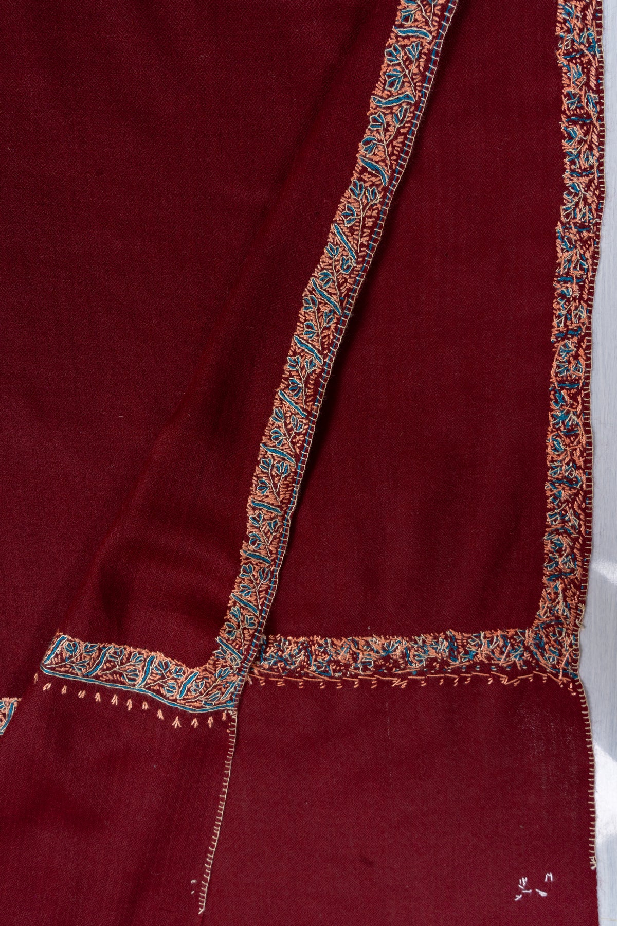 Folded ends of the maroon shawl showing narrow teal and beige embroidered borders