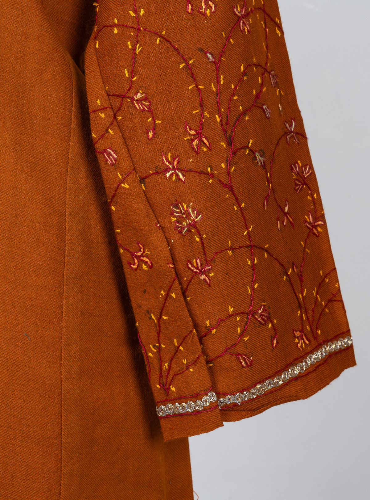 Sleeve detail of a burnt-orange pheran with fine red Sozni vines, gold leaves and pale embroidered cuff edging