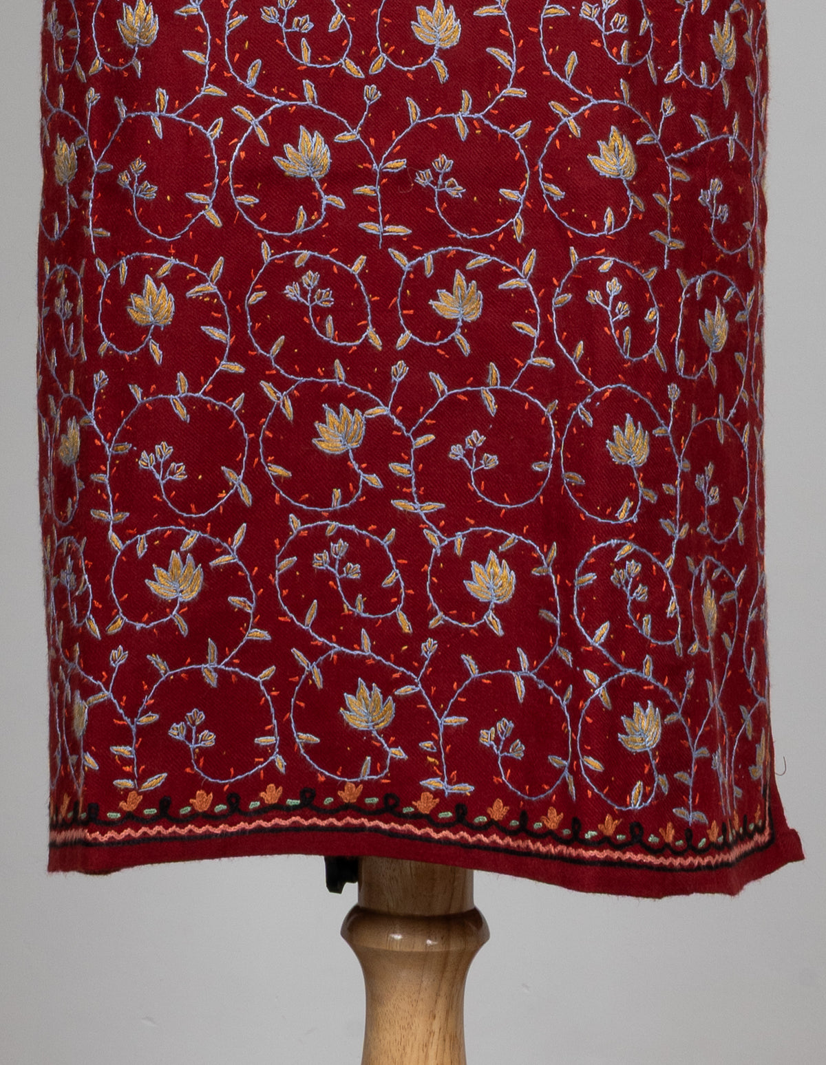 Lower front of a ruby pheran with fine Sozni floral vines above a dark embroidered hem border