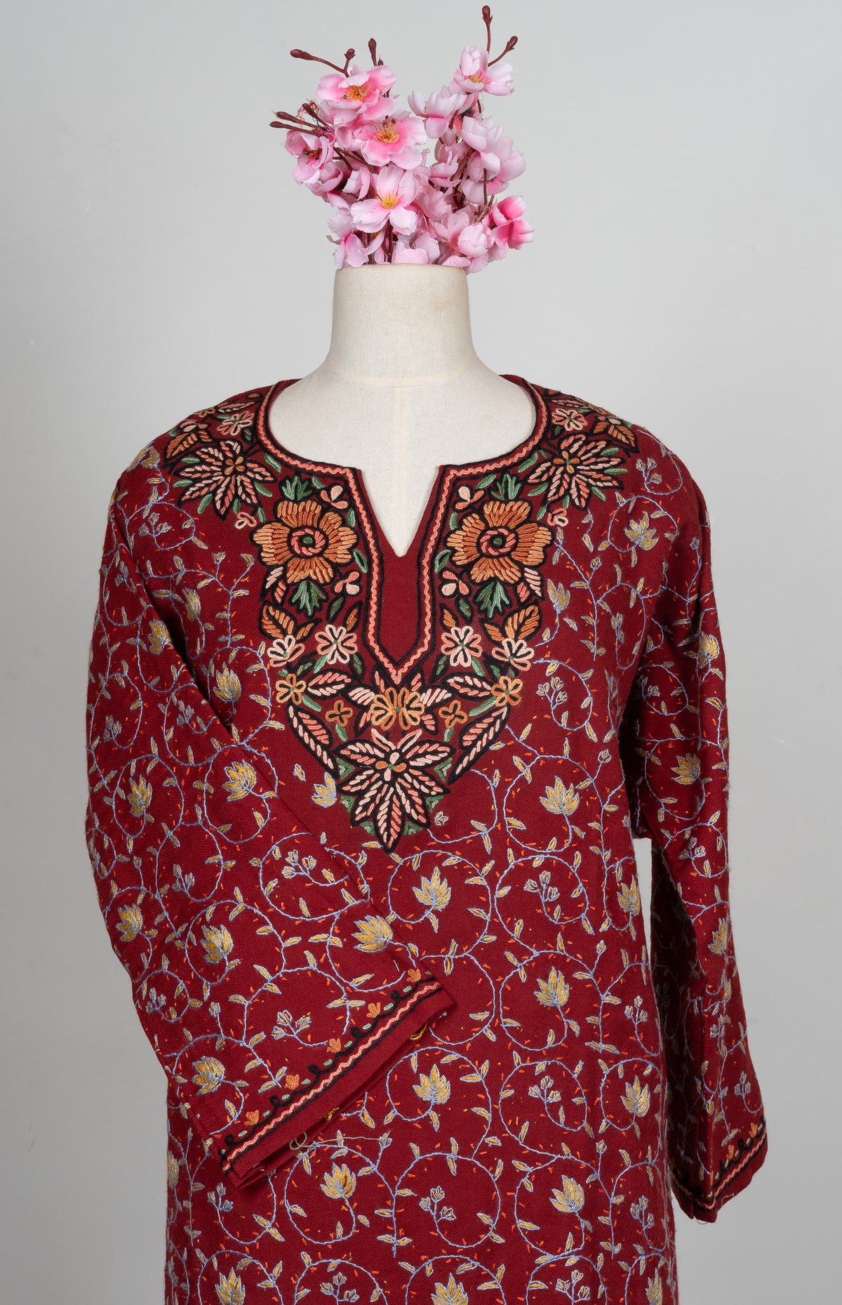 Upper front of a ruby pheran on a mannequin with fine Sozni floral vines and an ornate peach and green embroidered neckline