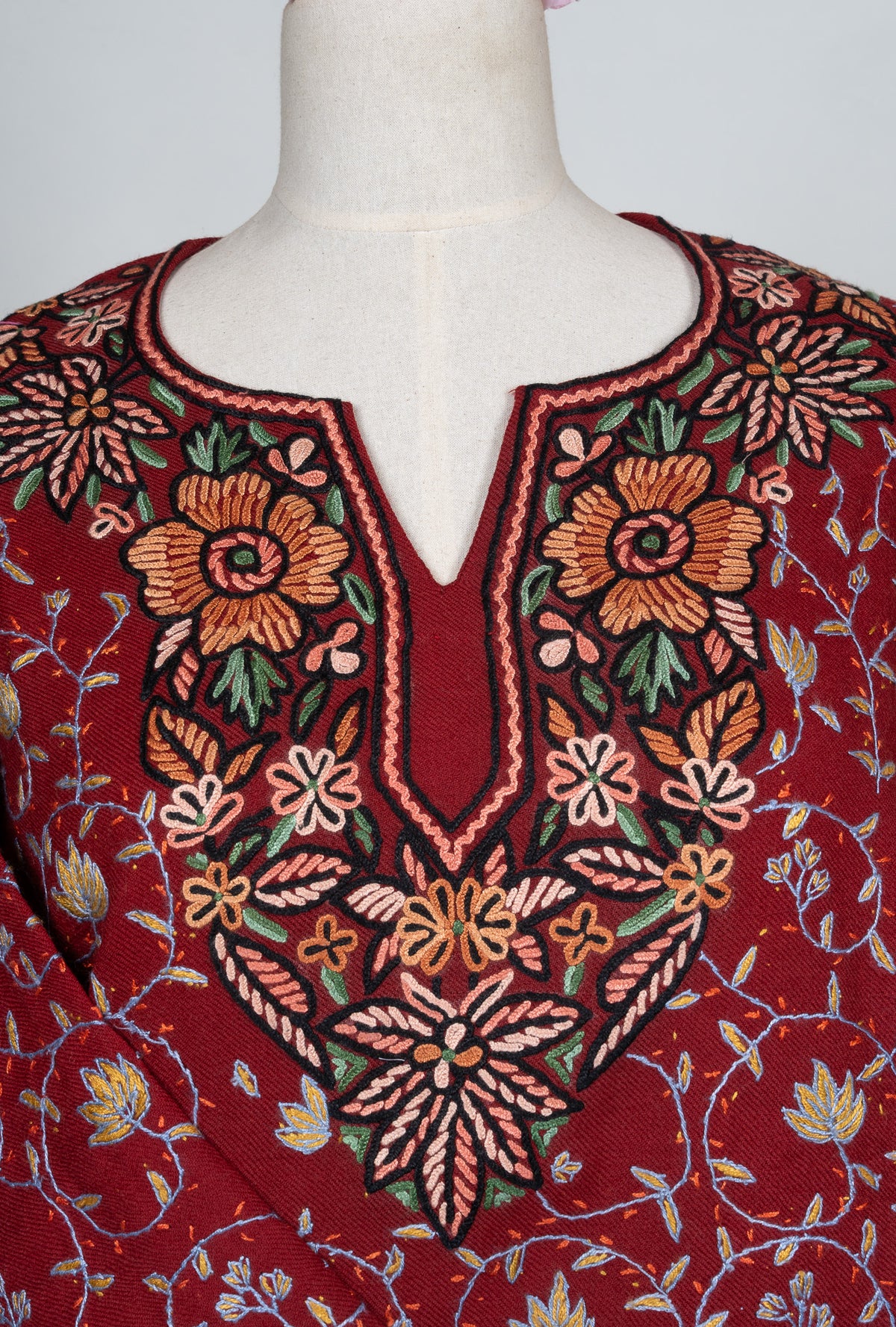 Close-up of peach flowers and green leaves around the ruby pheran's dark split-neckline panel