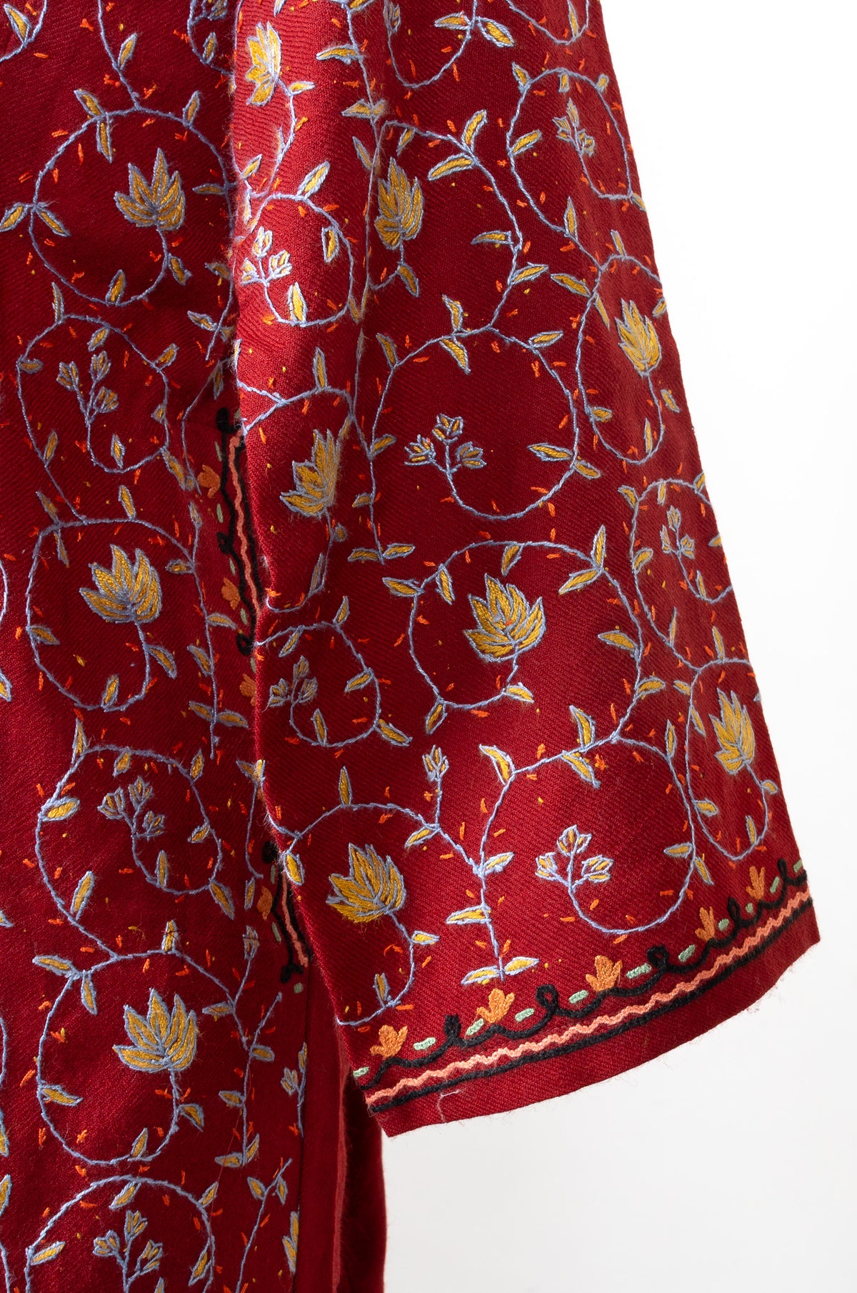 Sleeve detail of a ruby pheran with fine yellow and blue floral vines above dark cuff edging