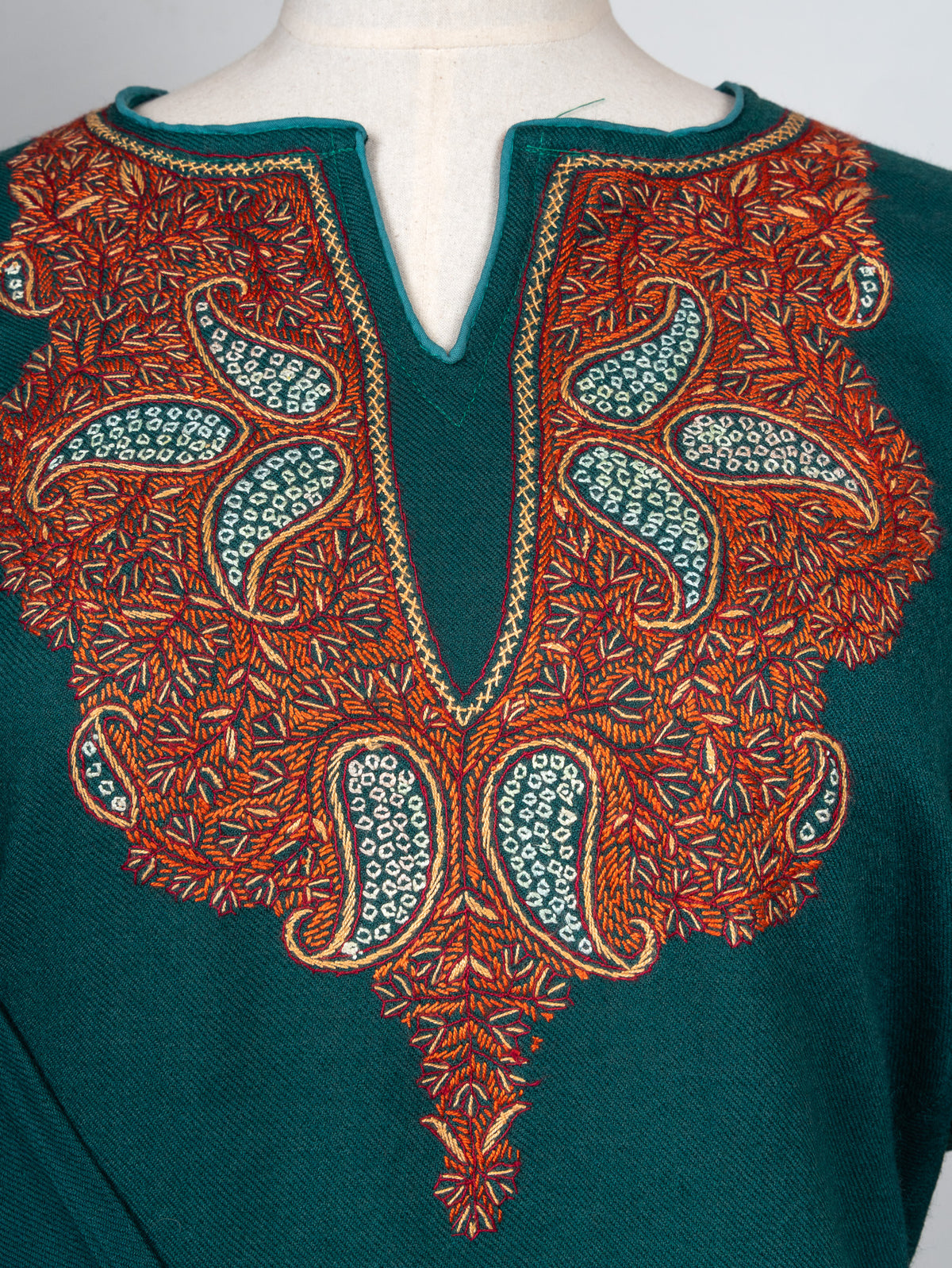 Close-up of a symmetrical copper-and-ivory paisley panel surrounding the notched neckline of a deep teal pheran