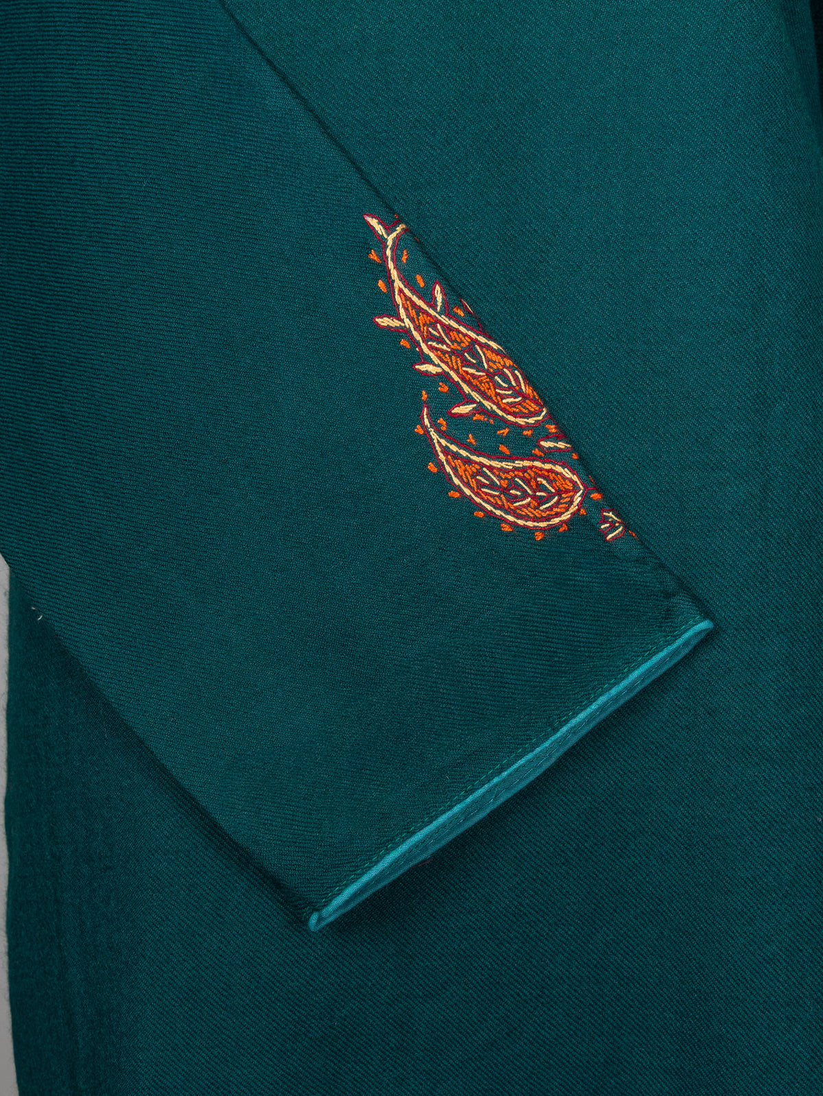 Crossed sleeve detail of a deep teal pheran with two copper paisleys near the cuff and narrow teal piping