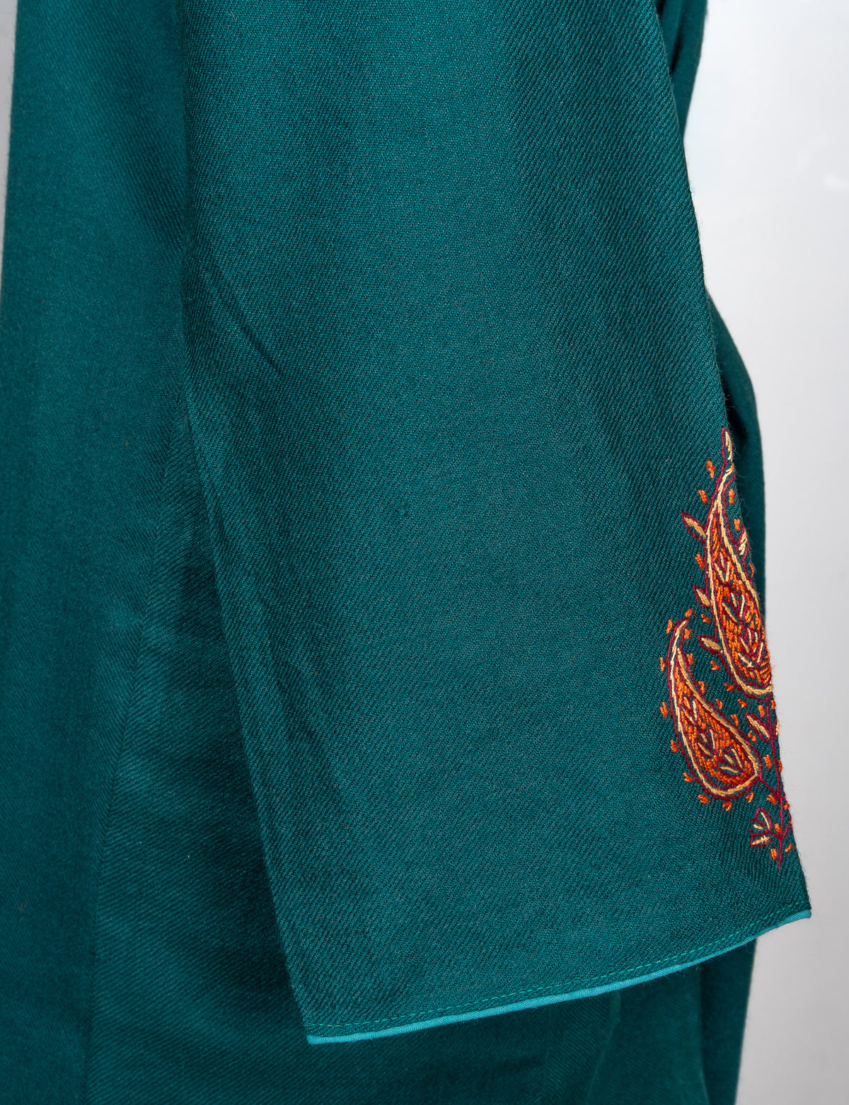 Hanging sleeve detail of a deep teal pheran showing copper paisley embroidery near the cuff