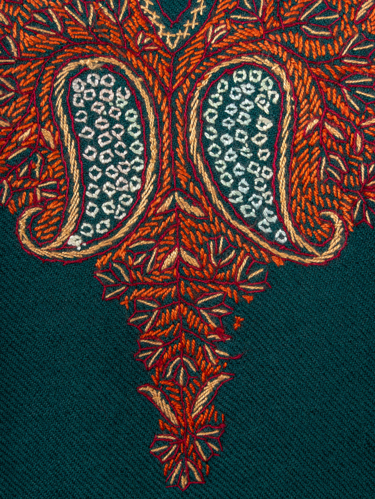 Macro detail of paired ivory-filled paisleys surrounded by copper leafy embroidery on the teal pheran's neckline panel