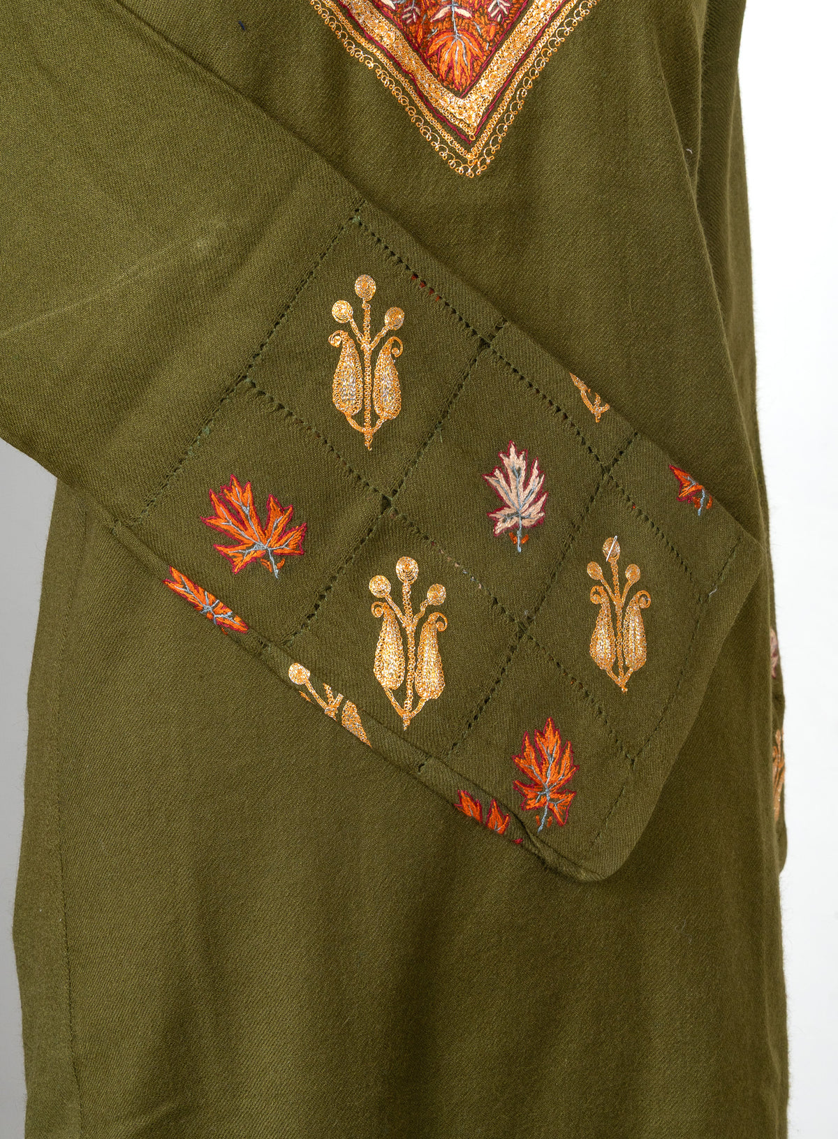 Angled cuff detail of an olive-green pheran with golden floral motifs and orange and pale pink leaves in a stitched grid