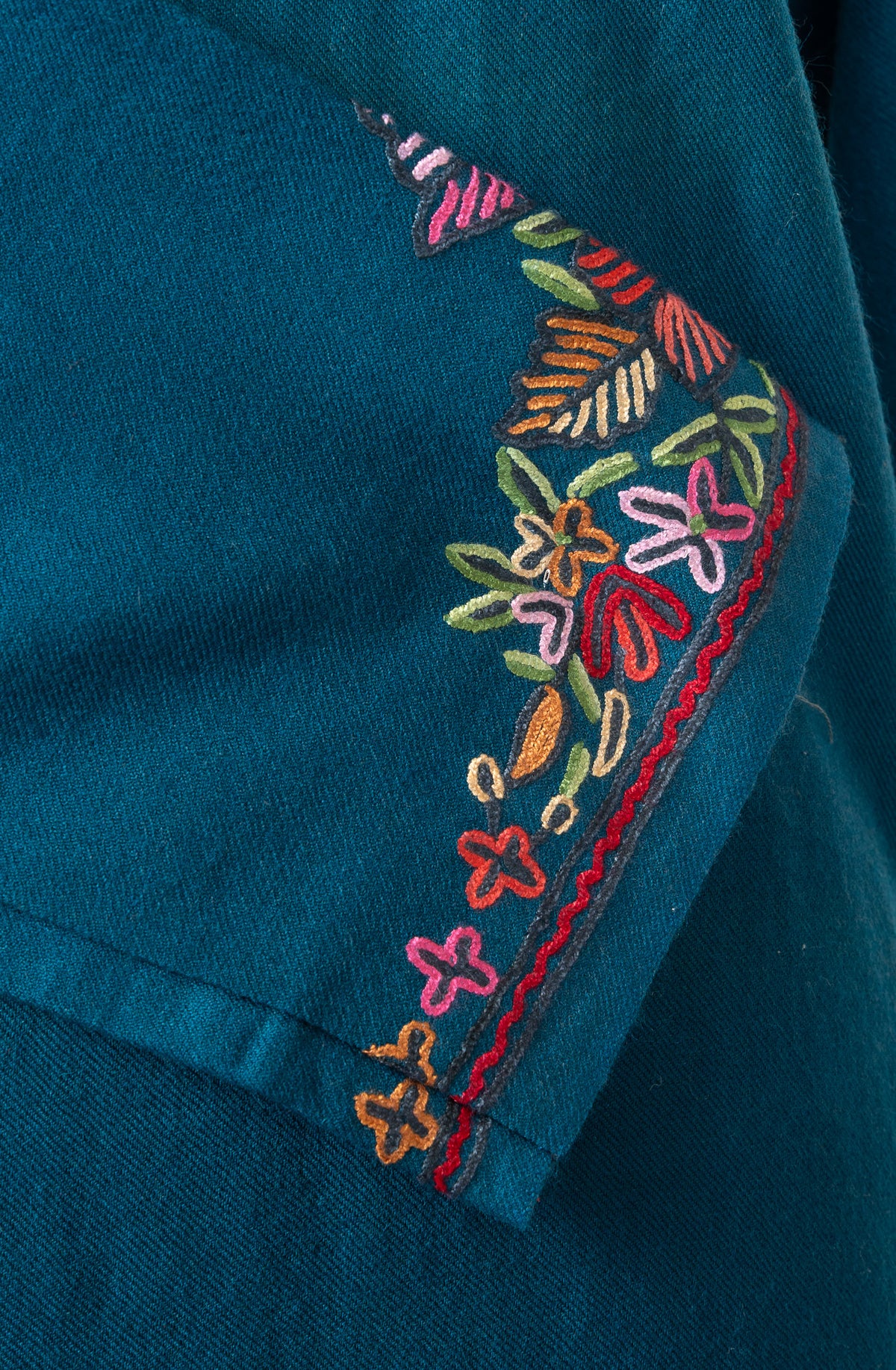 Close-up of colourful embroidered flowers and leaves along the crossed cuff of a teal pheran