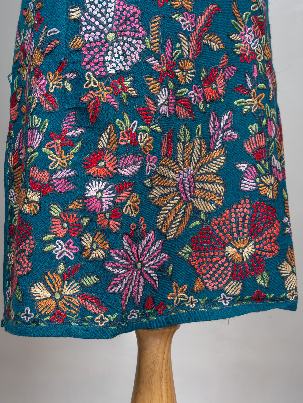 Lower front of a teal pheran with dense pink, red, orange and green floral embroidery above the hem