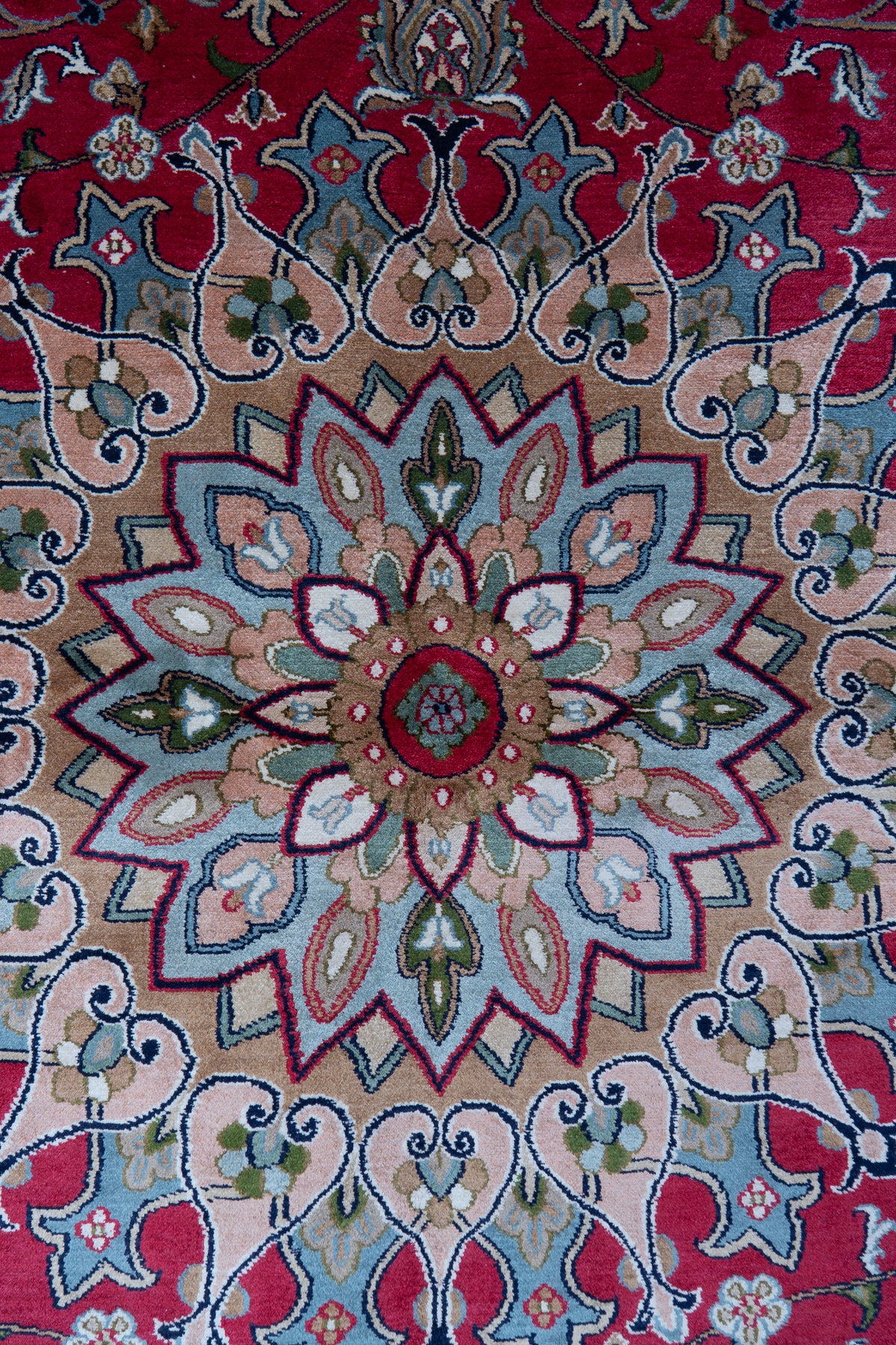 Close-up of the peach and pale blue petal medallion at the centre of a crimson mulberry silk carpet