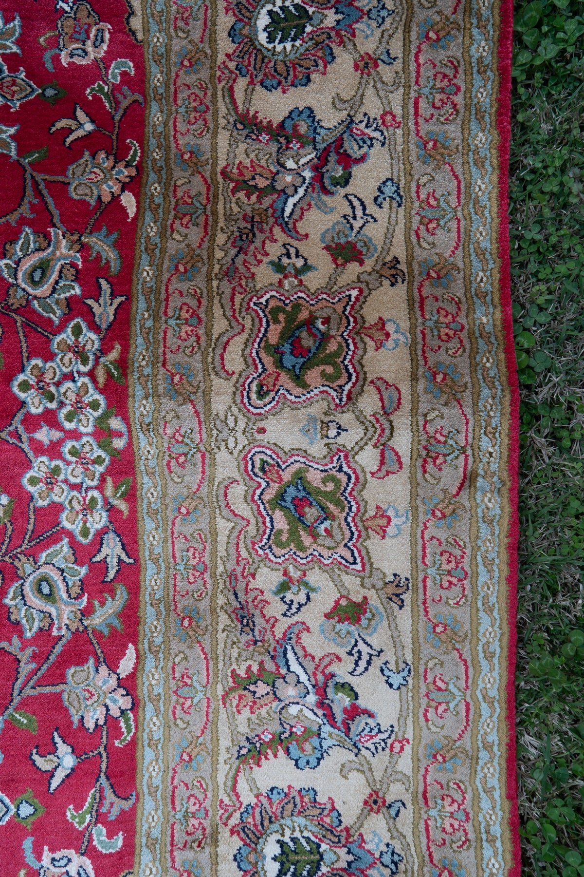 Close-up of the pale beige floral border beside the crimson field of a mulberry silk carpet
