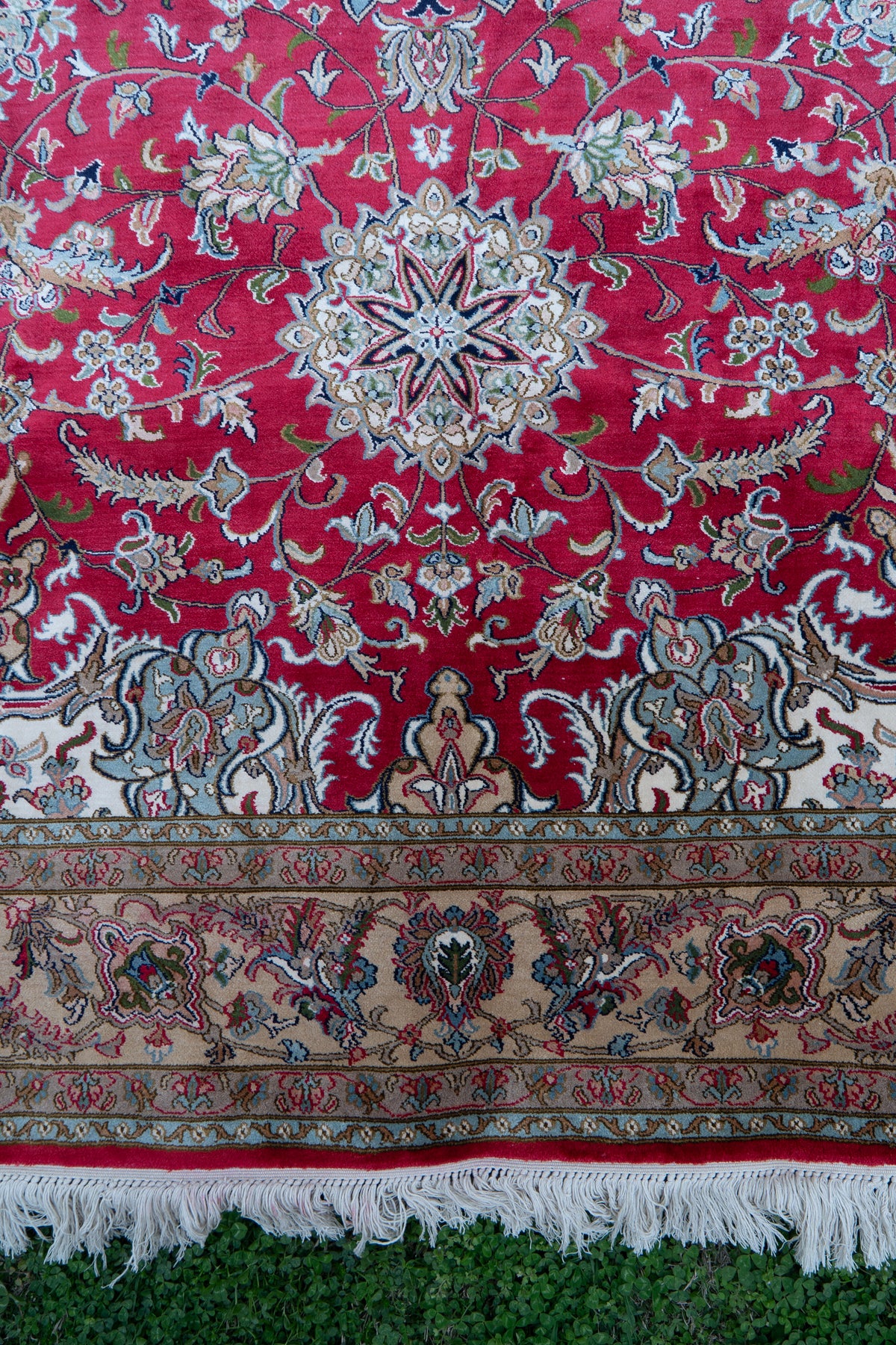 Lower section of a crimson mulberry silk carpet with pale floral motifs, a beige flower border and white fringe