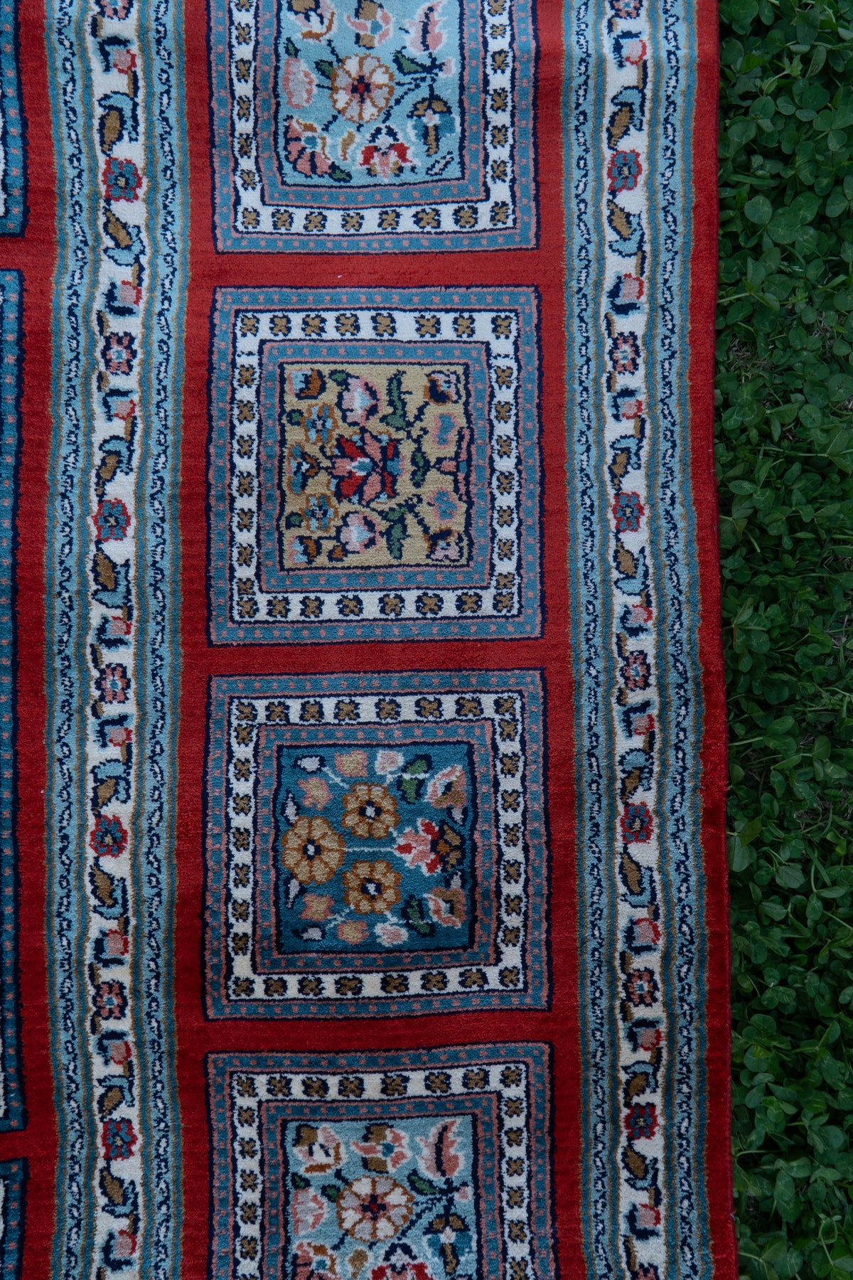 Detail of square floral panels along the carpet's crimson and blue side border
