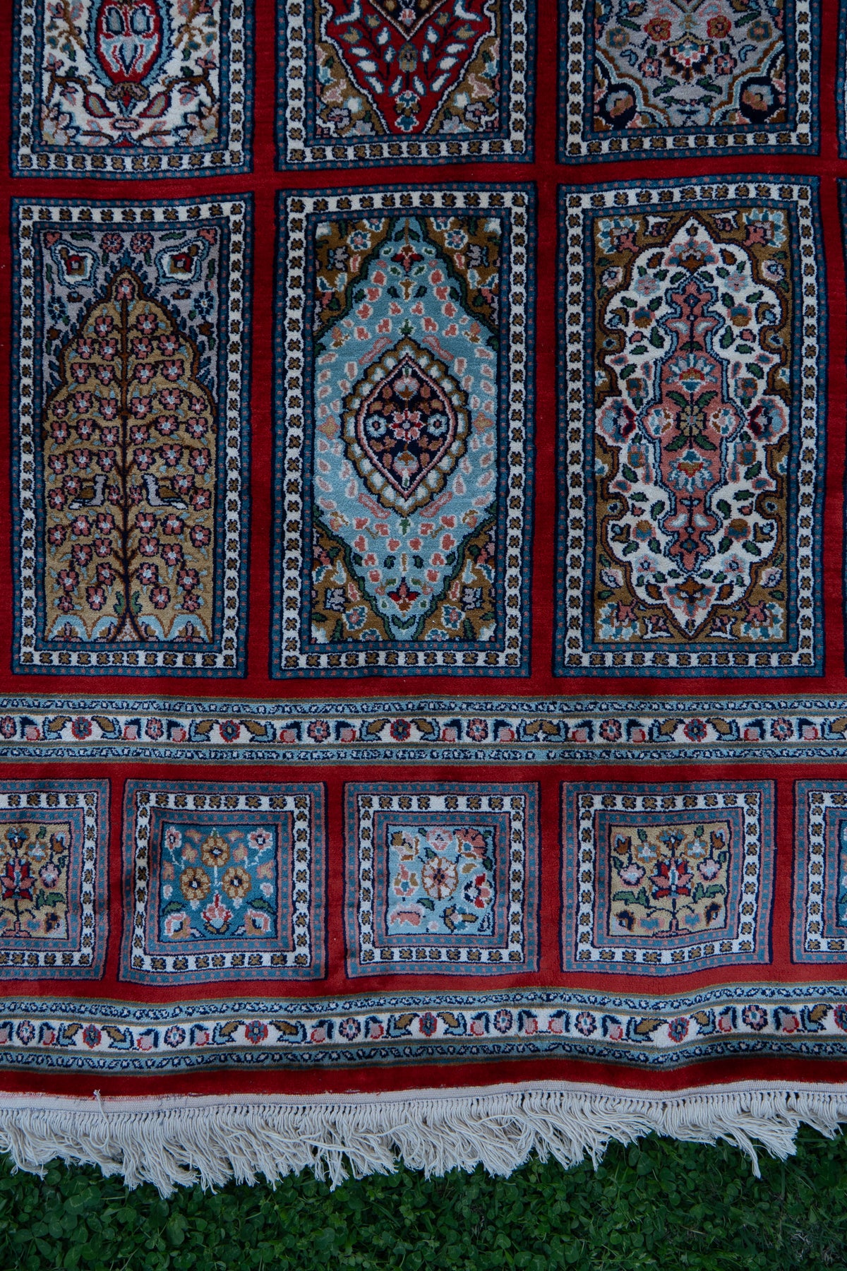 Lower section of the carpet with rectangular ornamental panels above a row of floral squares and white fringe