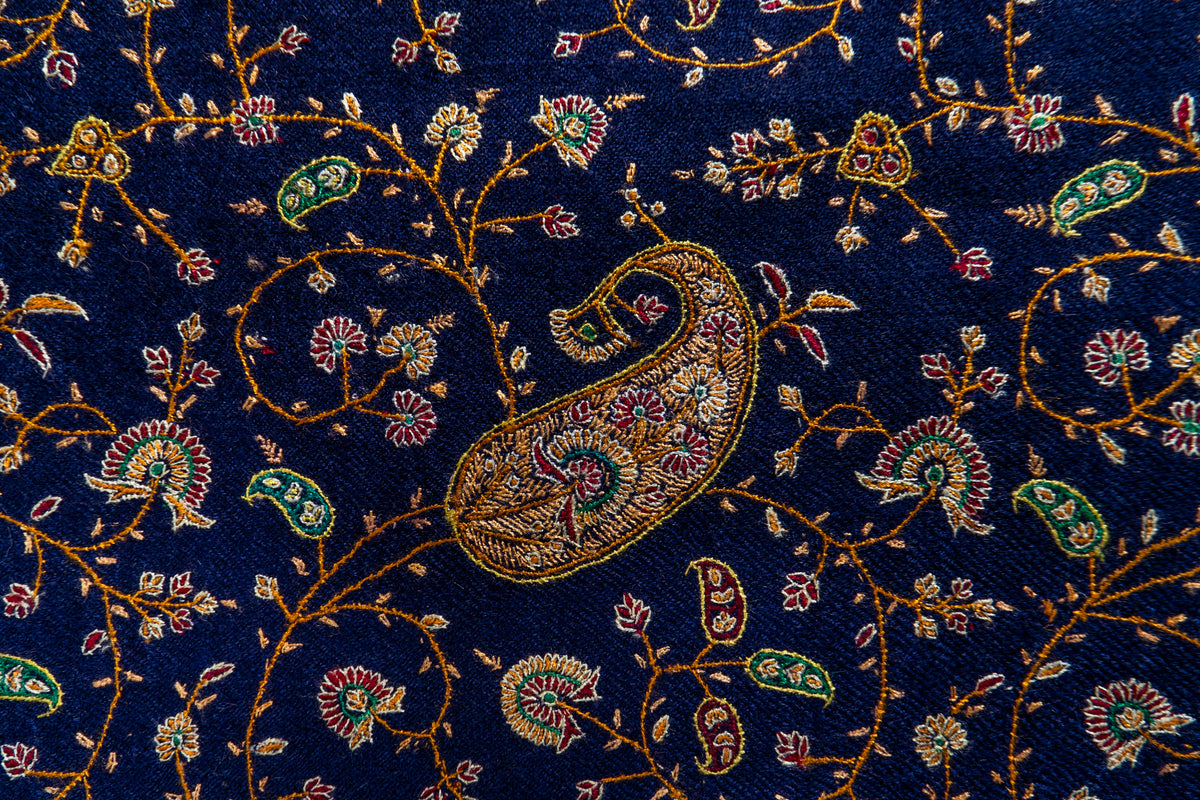 Close-up of a silk-thread Sozni paisley surrounded by gold, green and crimson floral vines on midnight-blue Pashmina