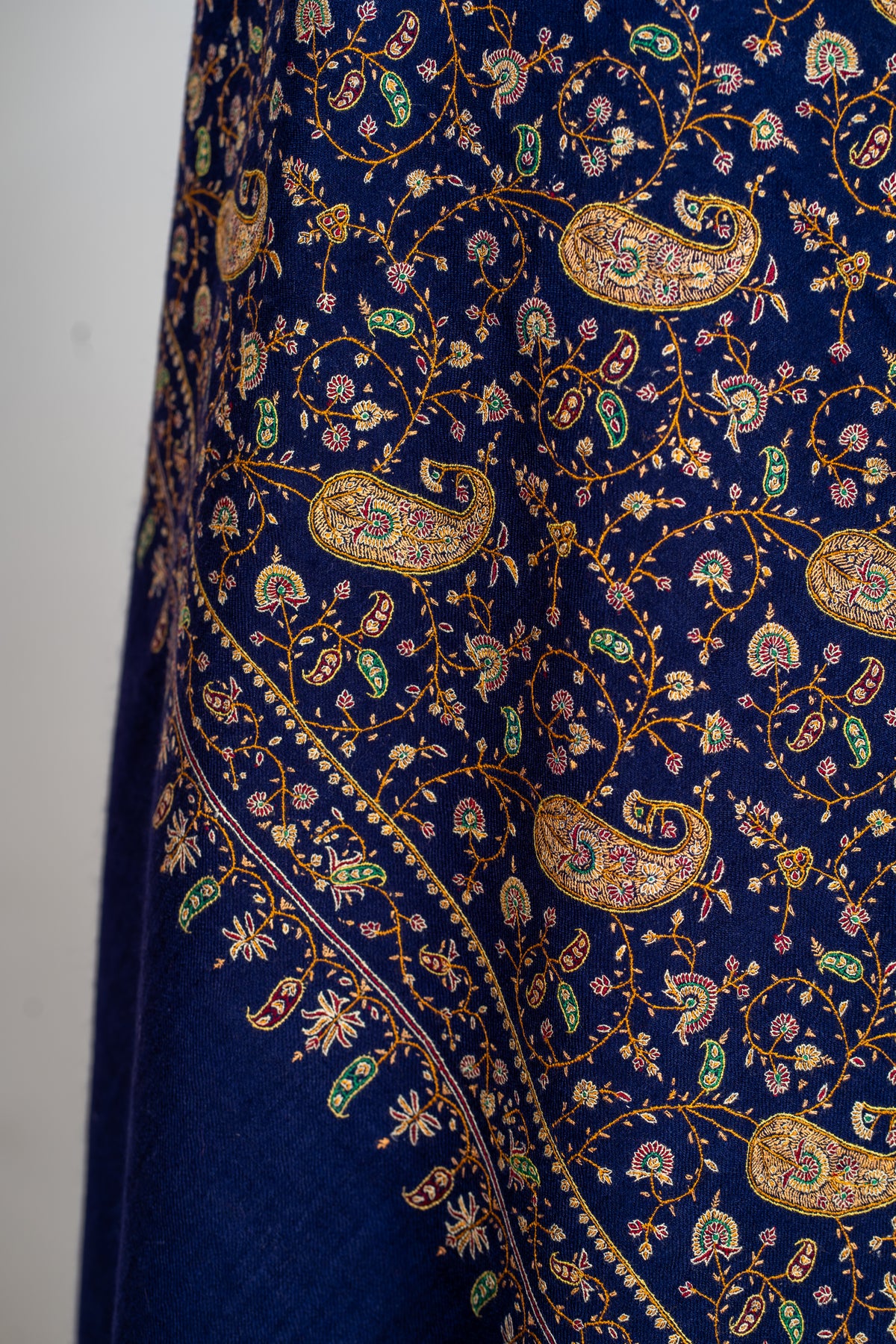 Close view of the blue shawl's hanging folds, with gold-toned paisleys and small green and crimson flowers
