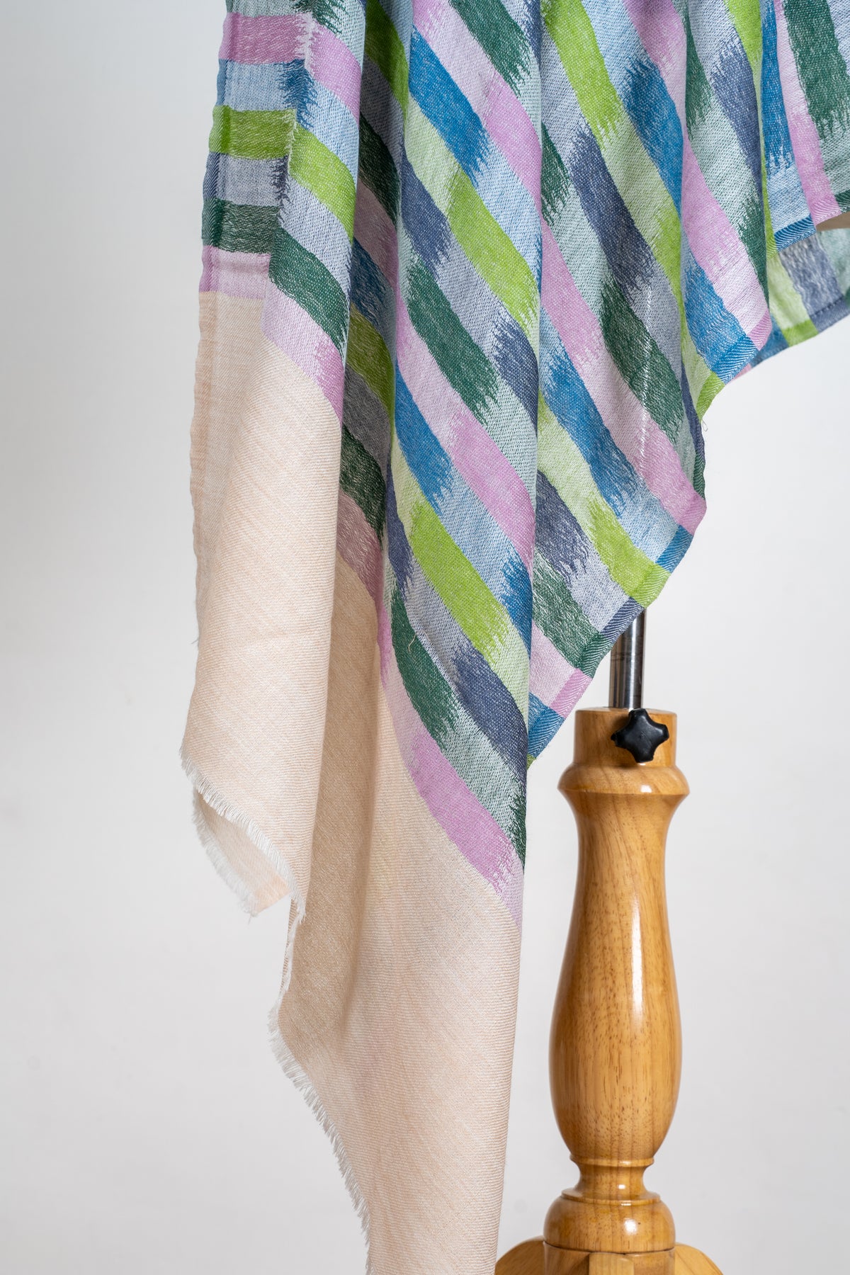 Hanging end of a printed Merino wool stole, with pink, blue and green blocks above a plain beige fringed panel