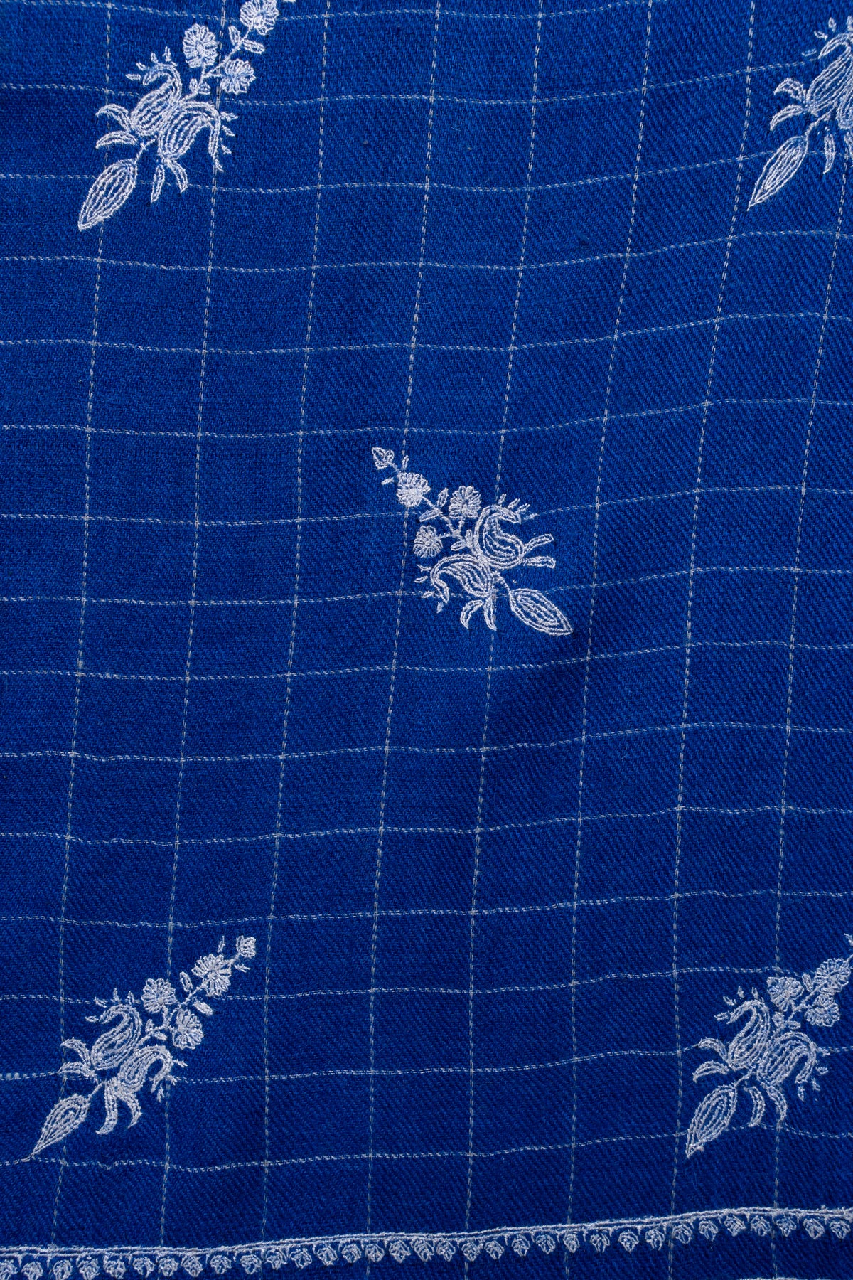 Close-up of white embroidered floral sprigs over fine checks on royal-blue Pashmina shawl