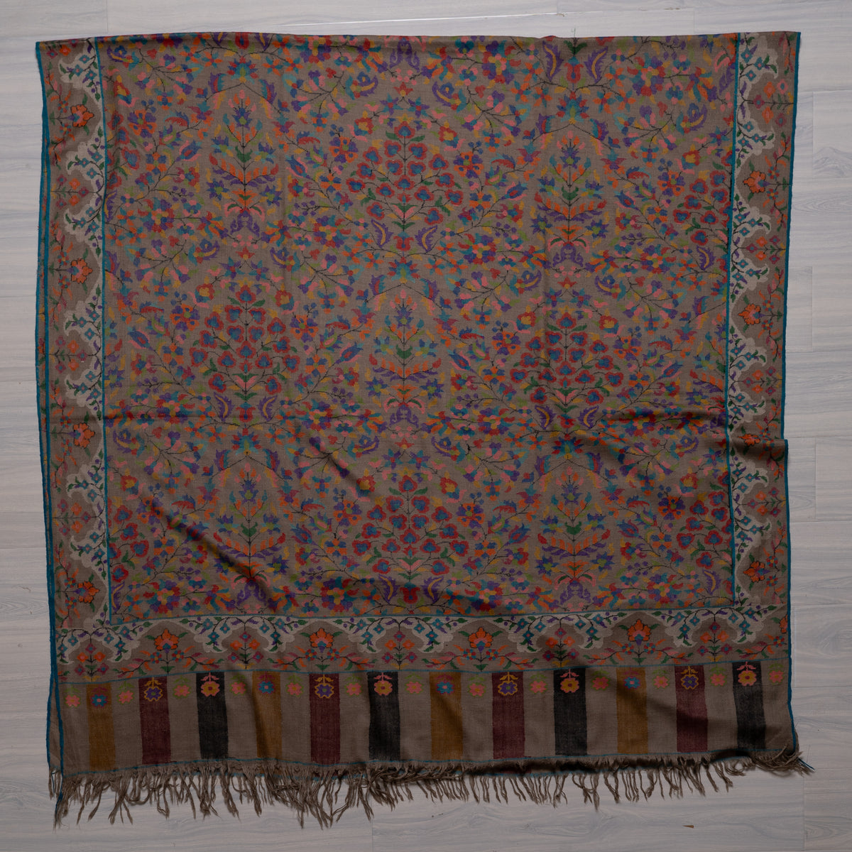 Taupe Pashmina shawl spread flat, with dense multicoloured flowers, broad floral borders and striped fringed ends