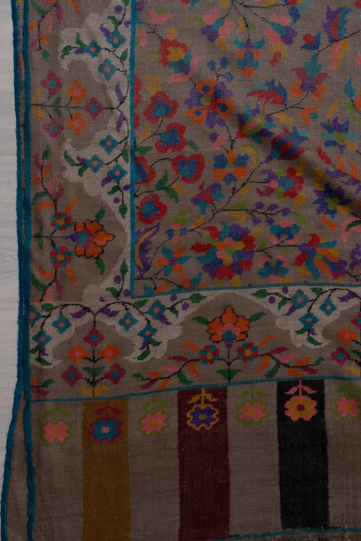 Corner detail of taupe Pashmina shawl showing colourful floral motifs, turquoise-edged borders and striped end panels