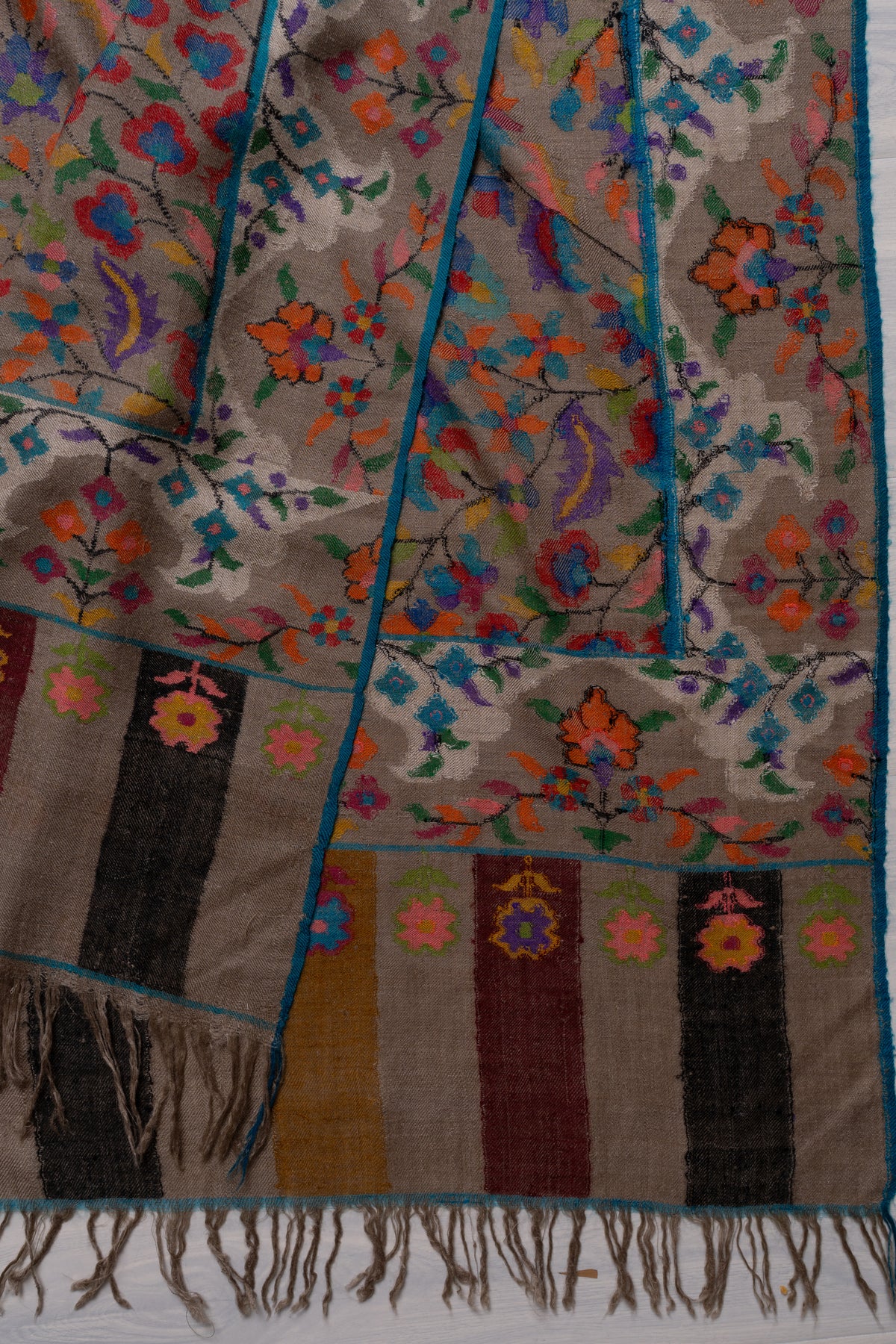 Folded corner of taupe Pashmina shawl with colourful floral borders, striped end panels and taupe fringe