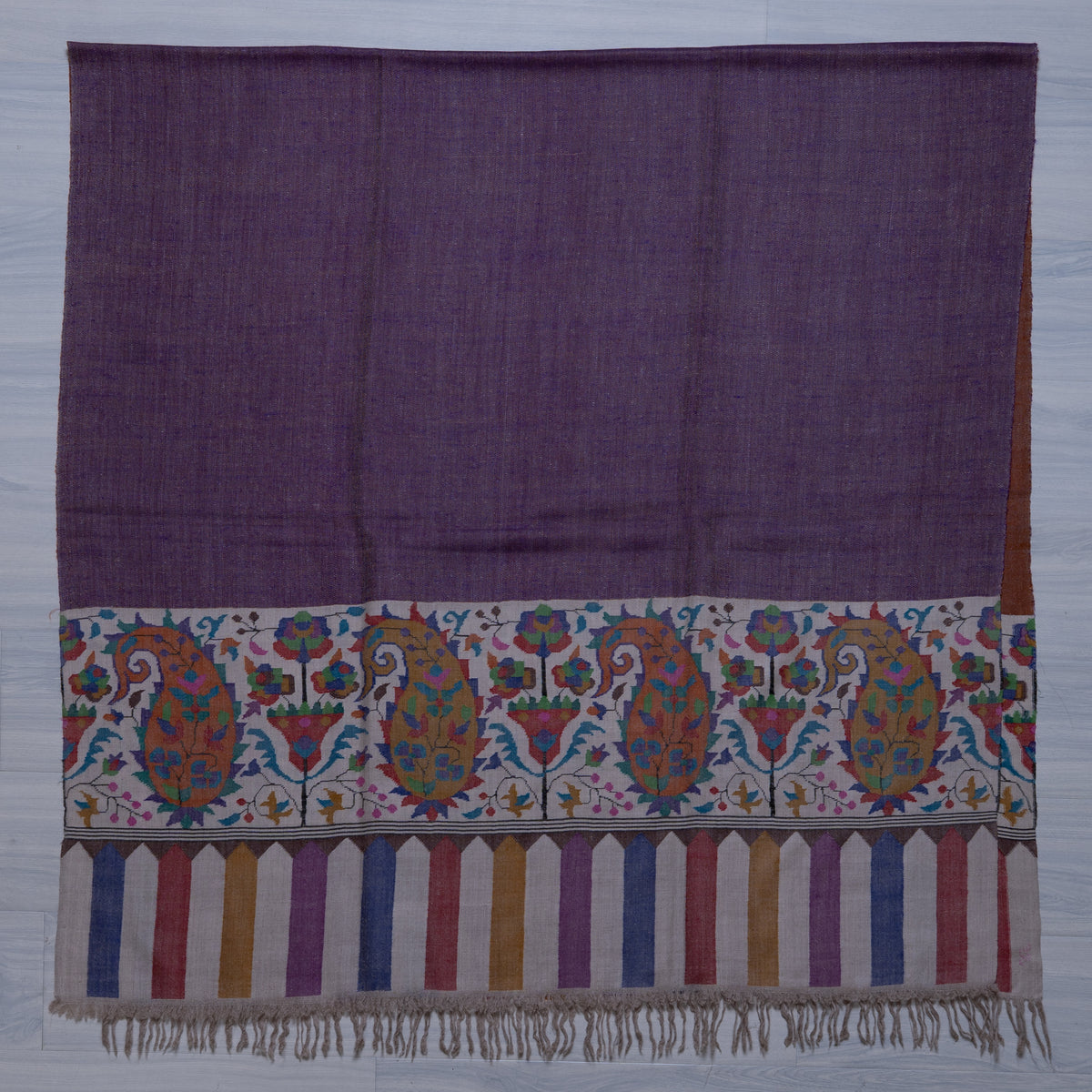 Purple Pashmina shawl spread flat, showing a plain field above an ivory paisley-and-flower panel, striped tips and ivory fringe.