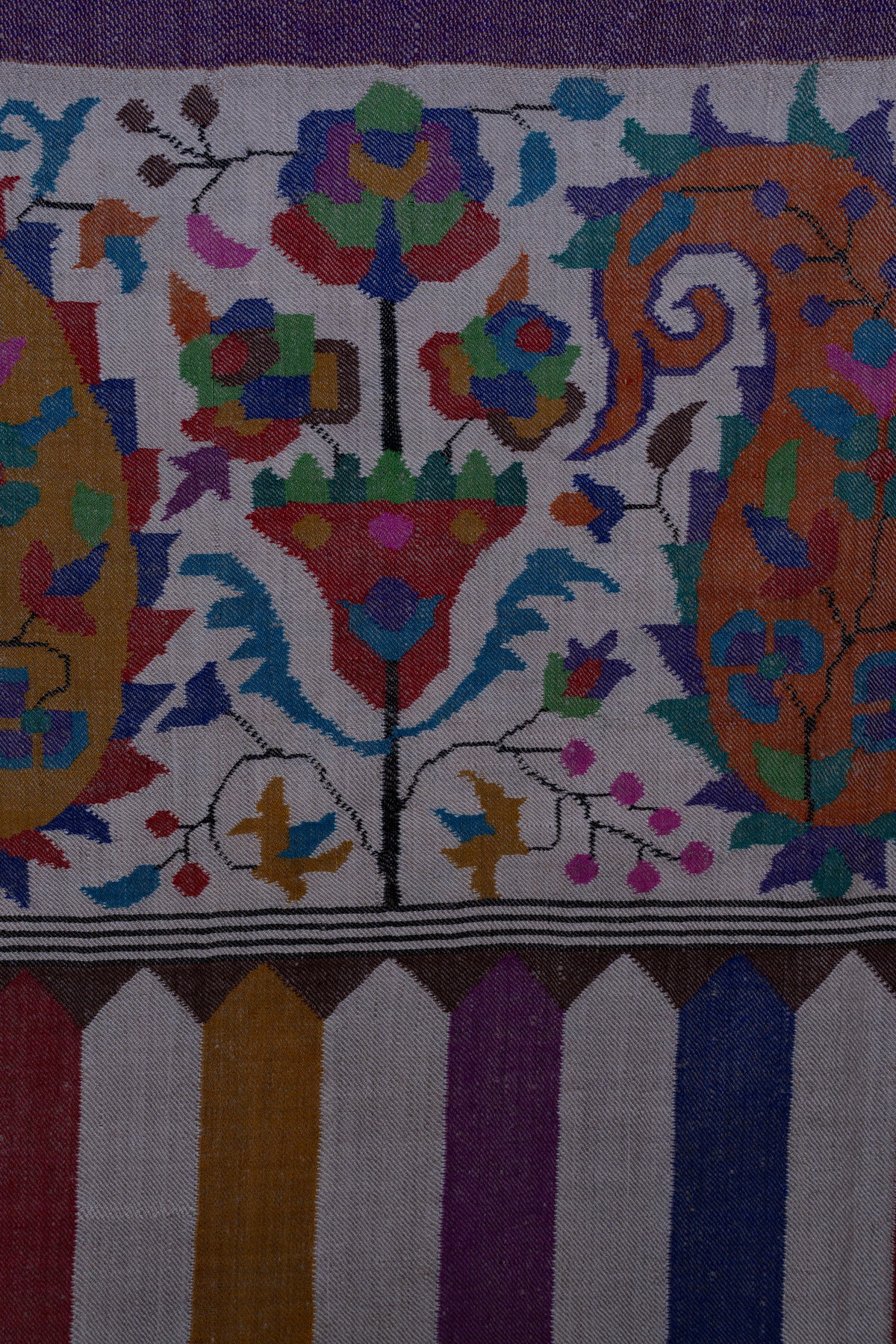 Close-up of colourful flowers and orange paisleys on the Pashmina shawl's ivory end panel above purple, blue, red and gold stripes.