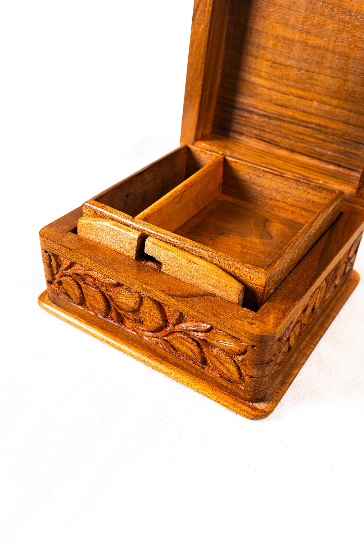 Close-up of the open box’s divided wooden tray, polished lid interior and carved floral front.