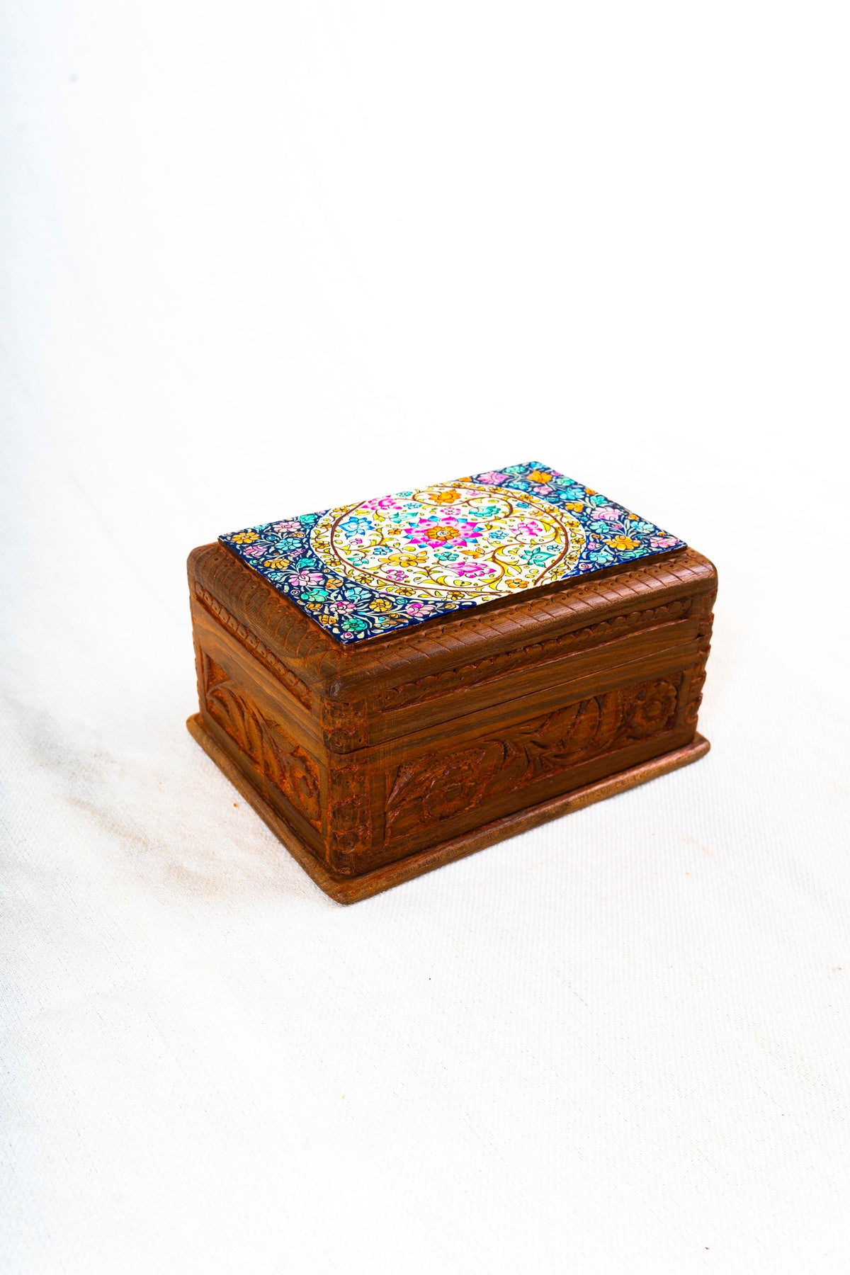 Closed walnut wood box seen from above at an angle, with a colourful floral papier-mâché top and carved sides