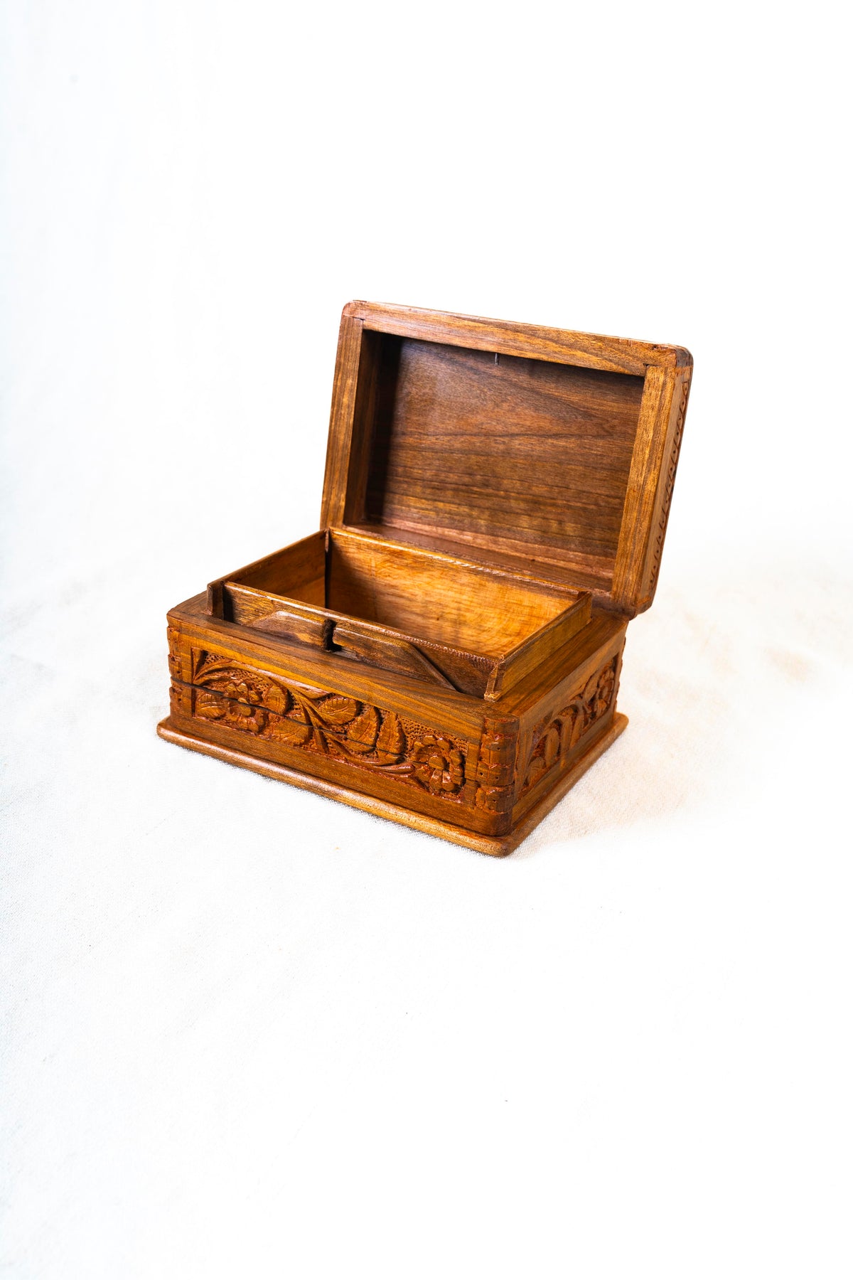 Open walnut wood box at an angle, showing its plain wooden interior, hinged lid and carved floral sides