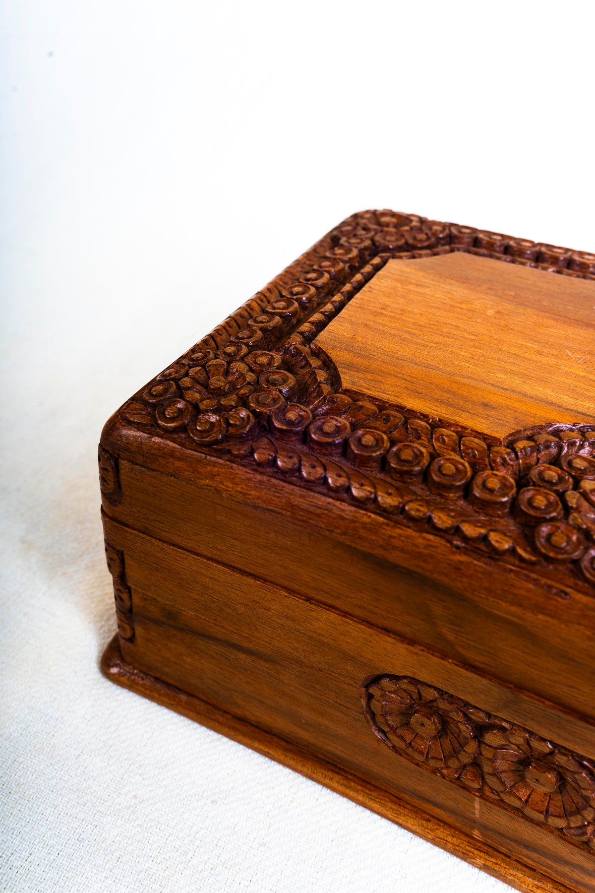 Angled detail of the walnut box corner, showing raised floral lid carving and a small side medallion.