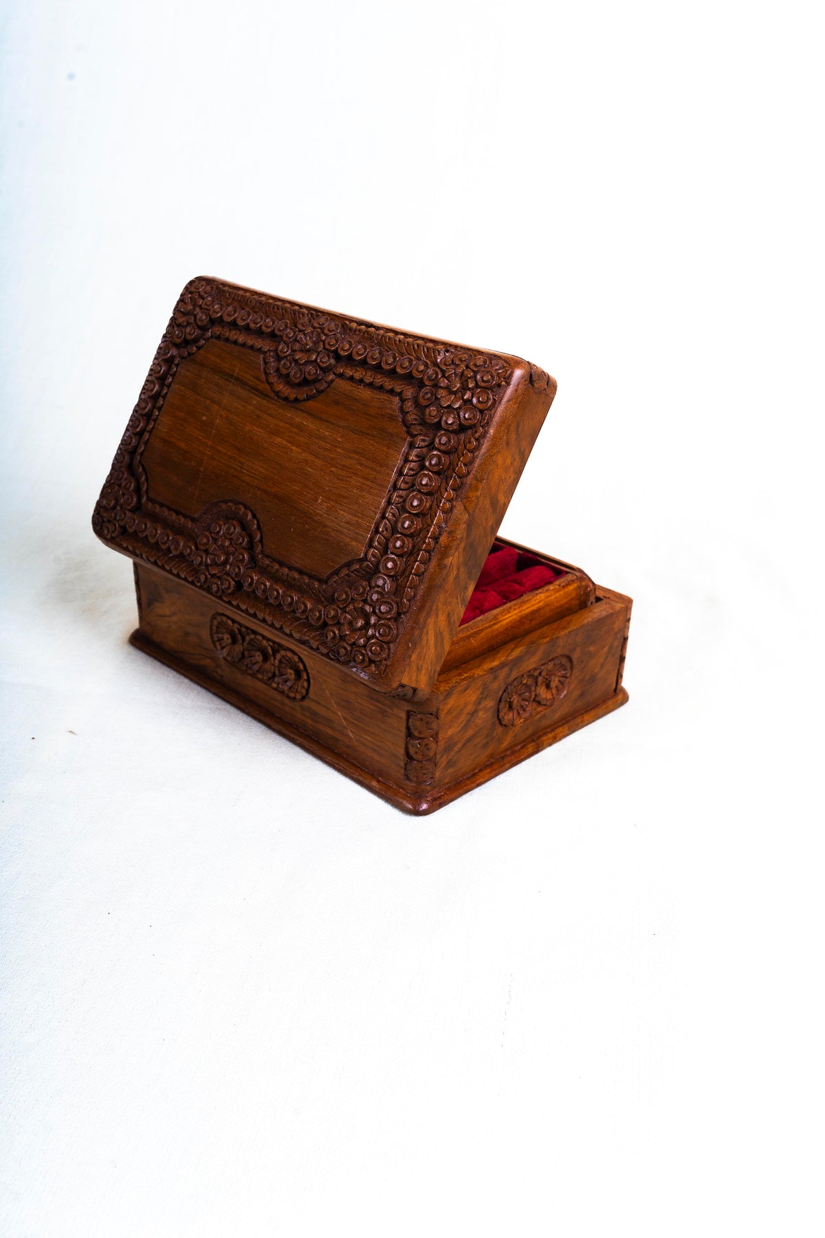 Opposite rear angle of the open walnut box, with the carved lid exterior and red lining visible at the side.