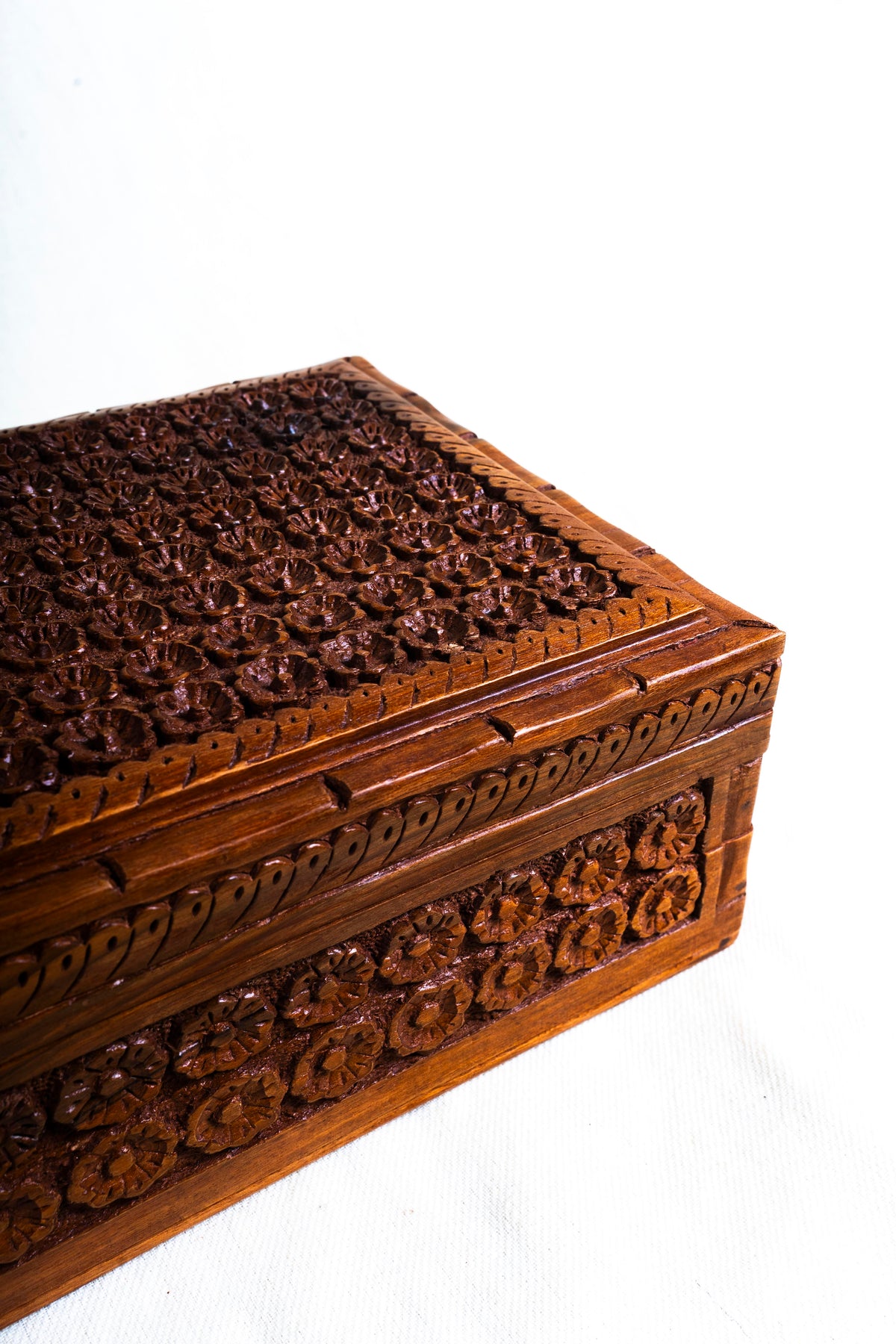 Close side view of the closed walnut box showing rows of carved flowers and decorative trim around the lid