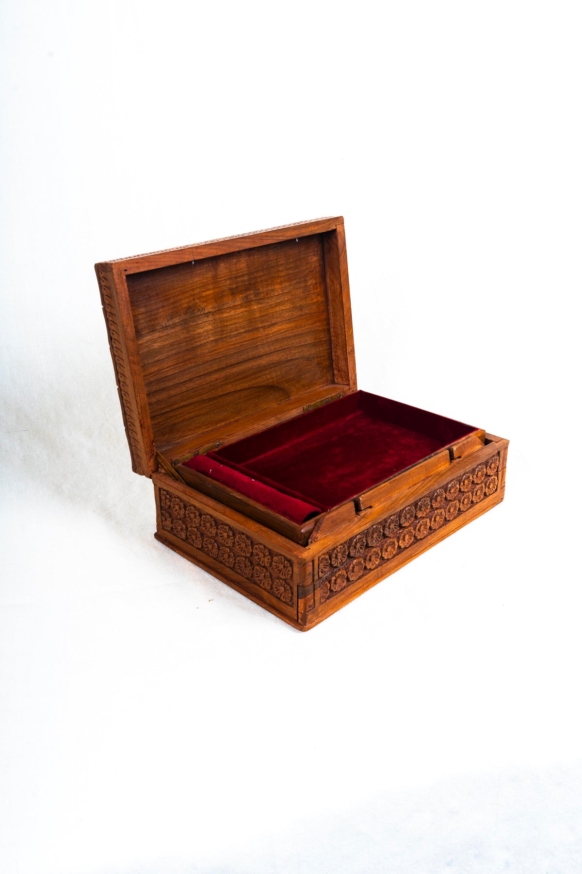 Angled view of the open walnut box with red velvet lining and dense floral carving across the exterior