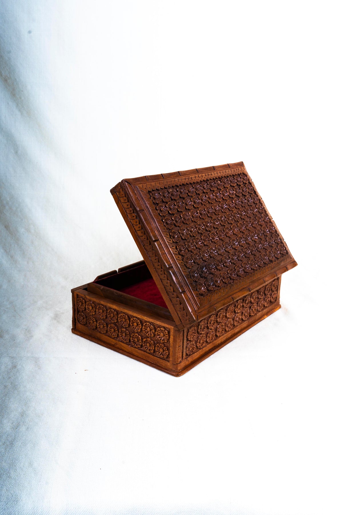 Walnut box with its floral-carved lid partly raised above the red velvet interior