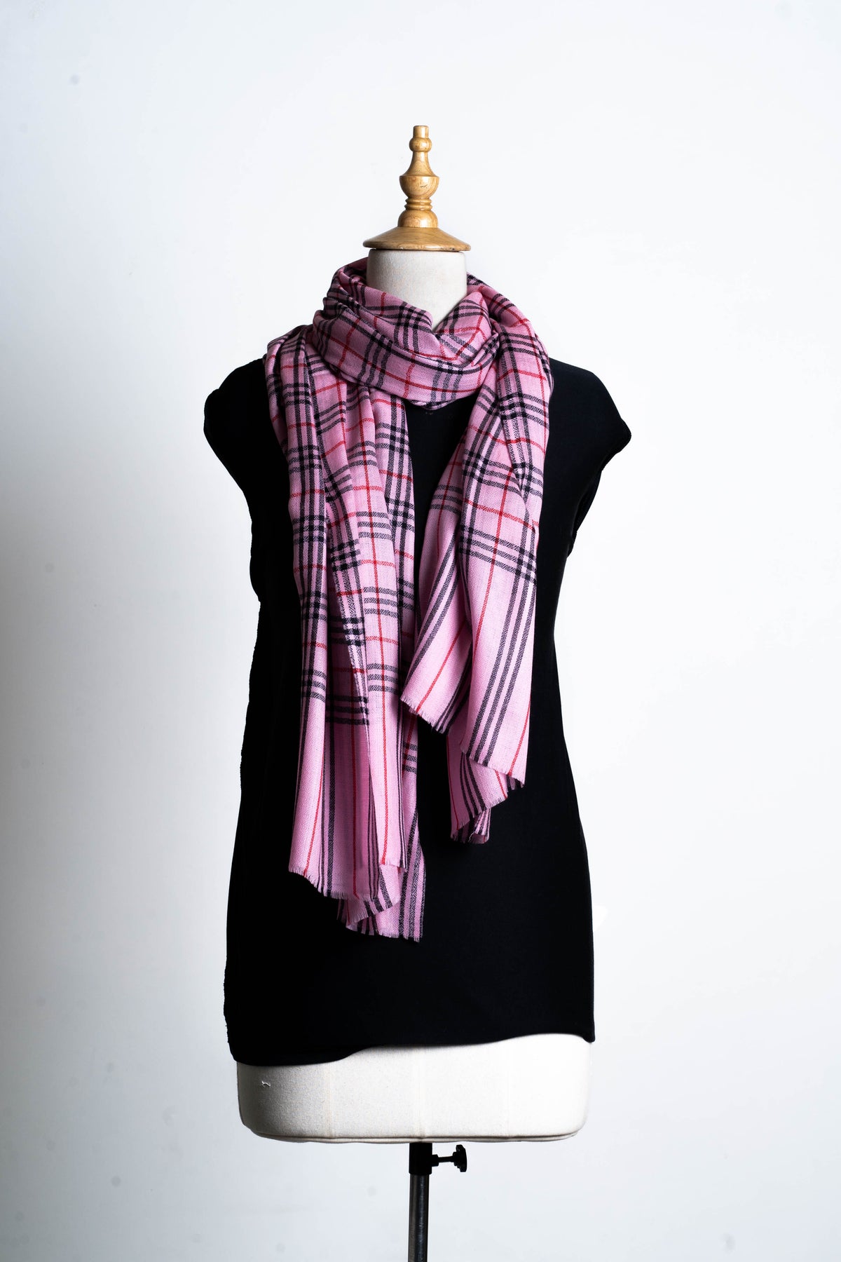 Full view of a pink checked Merino wool stole looped around a mannequin in a black top, with uneven hanging ends