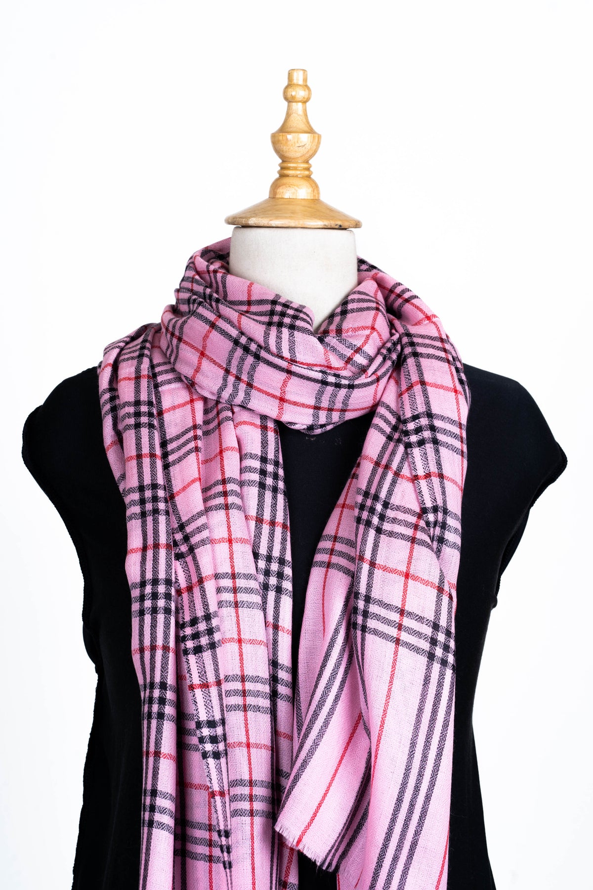 Upper view of a pink Merino wool stole wrapped around a mannequin's neck, showing black and red checks and striped tails