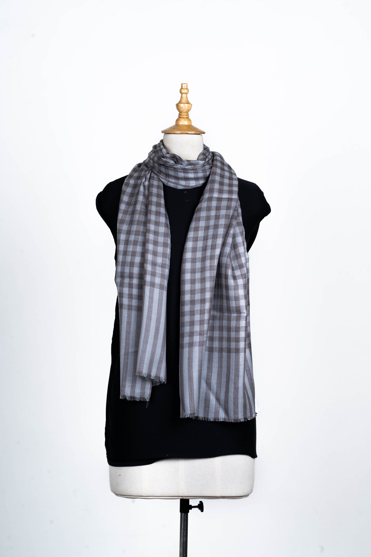 Full front view of the grey checked stole draped around a mannequin neck, ending in striped panels with short fringe.