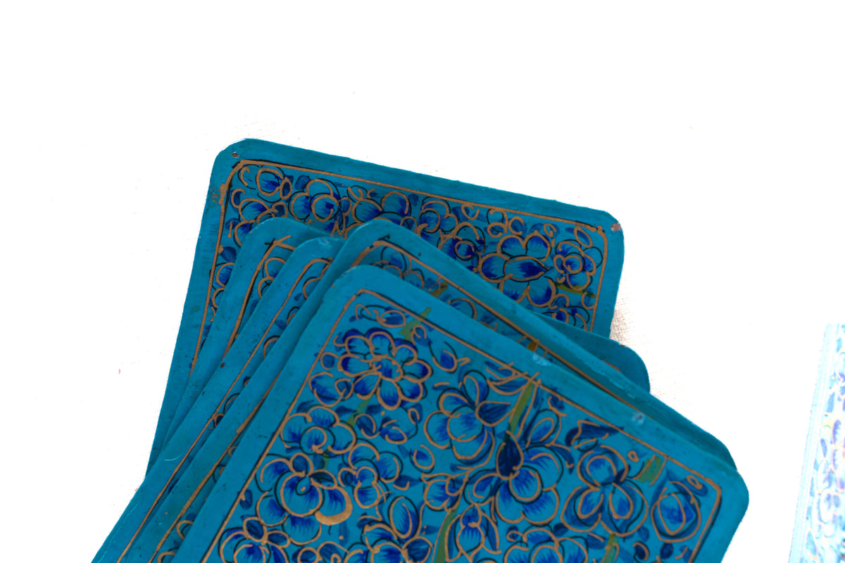Close-up of stacked blue coasters painted with curling gold outlines and dark blue flowers