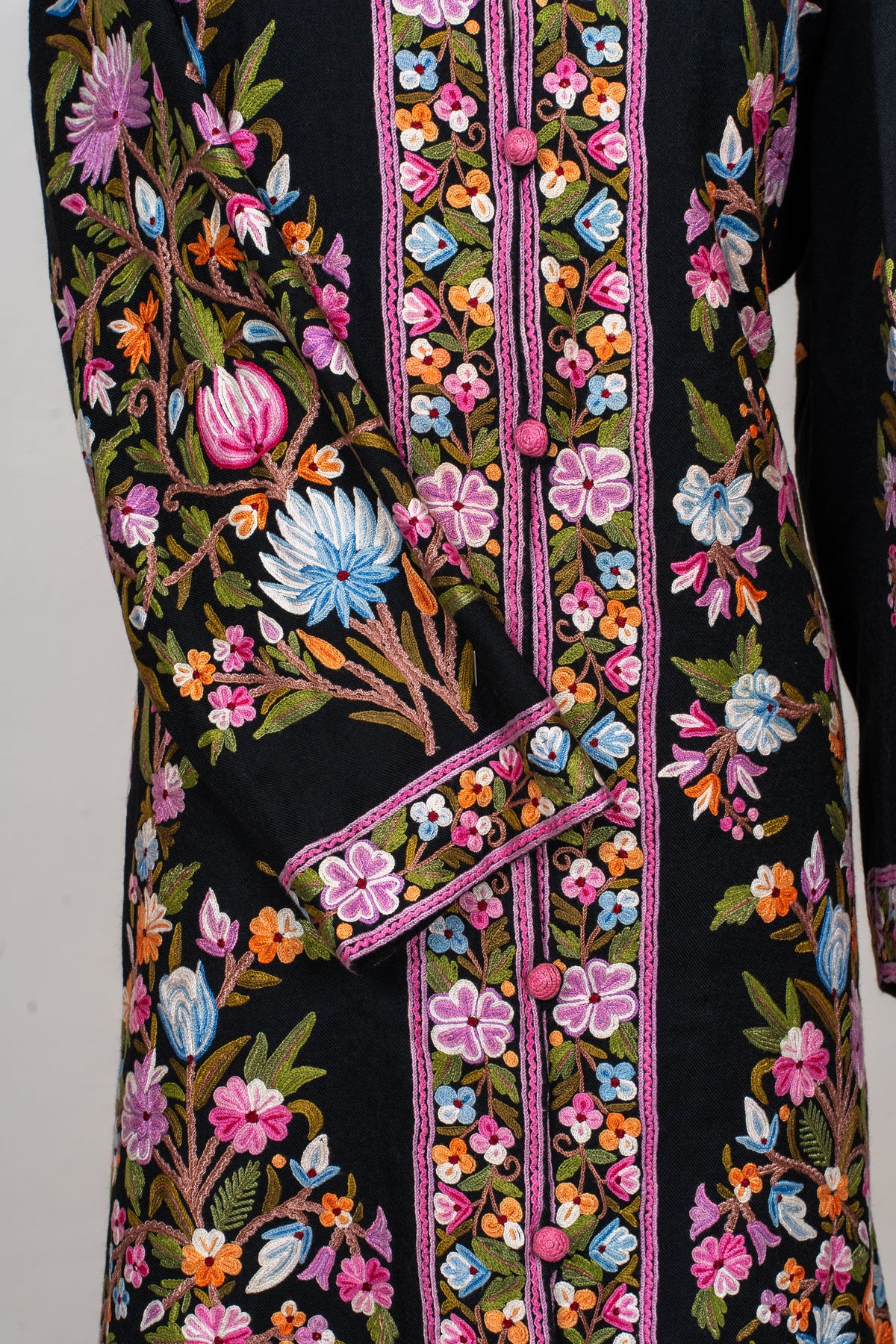 Detail of the jacket’s crossed sleeve and floral cuff beside pink covered buttons and embroidered front borders